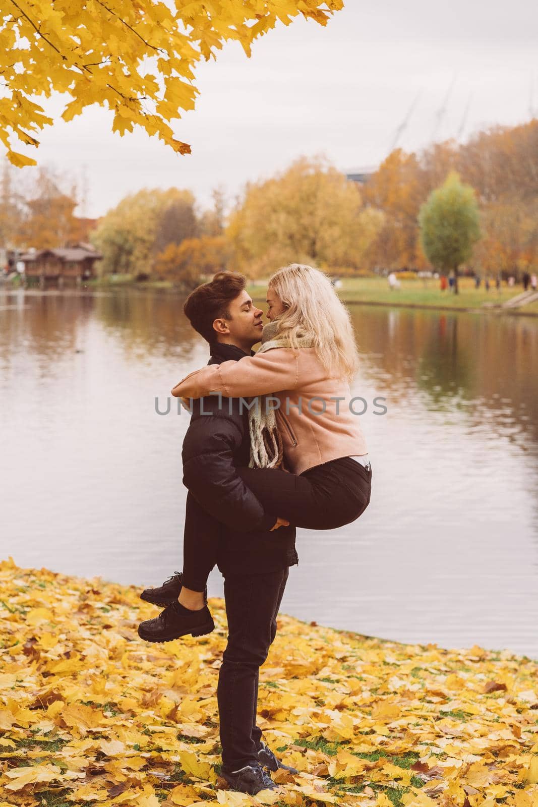 Cute brunette guy holds in his arms and kisses a beautiful blonde girl. Loving teens are happy, smiling, kissing. The concept of teenage love walking outdoors, vertical