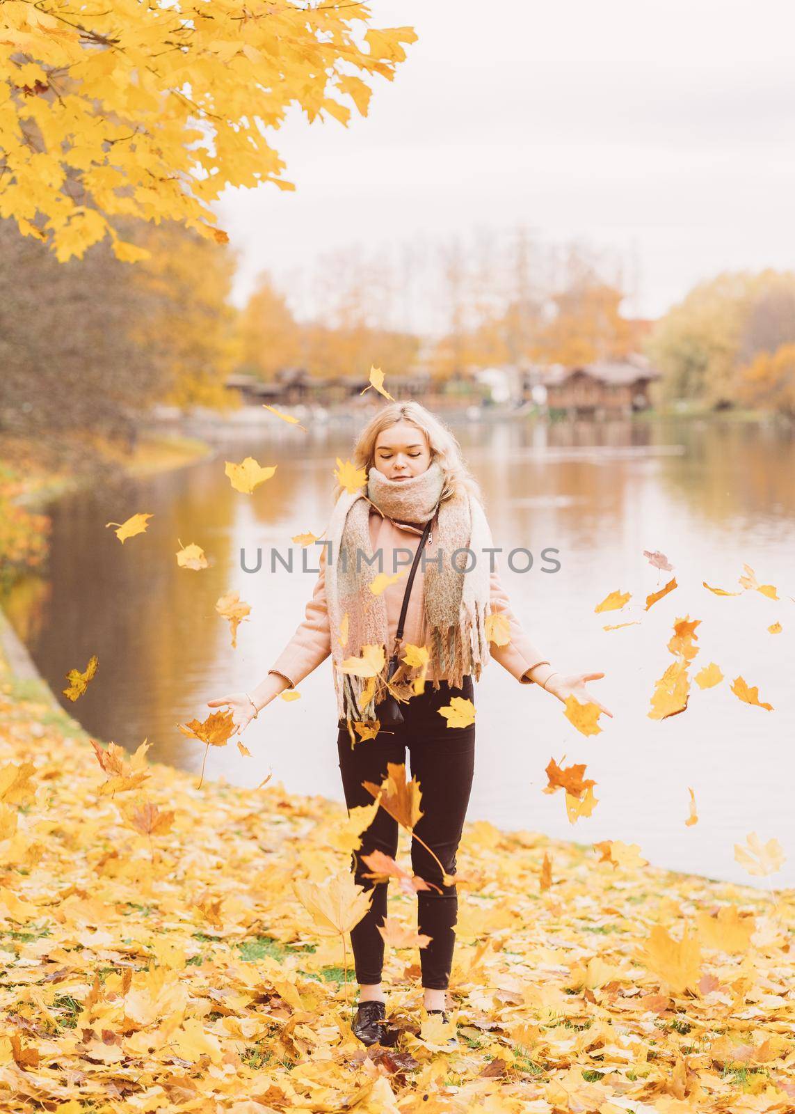 Beautiful young girl throws up autumn leaves. Attractive young woman is resting, fooling around, playing with leaves in a park.