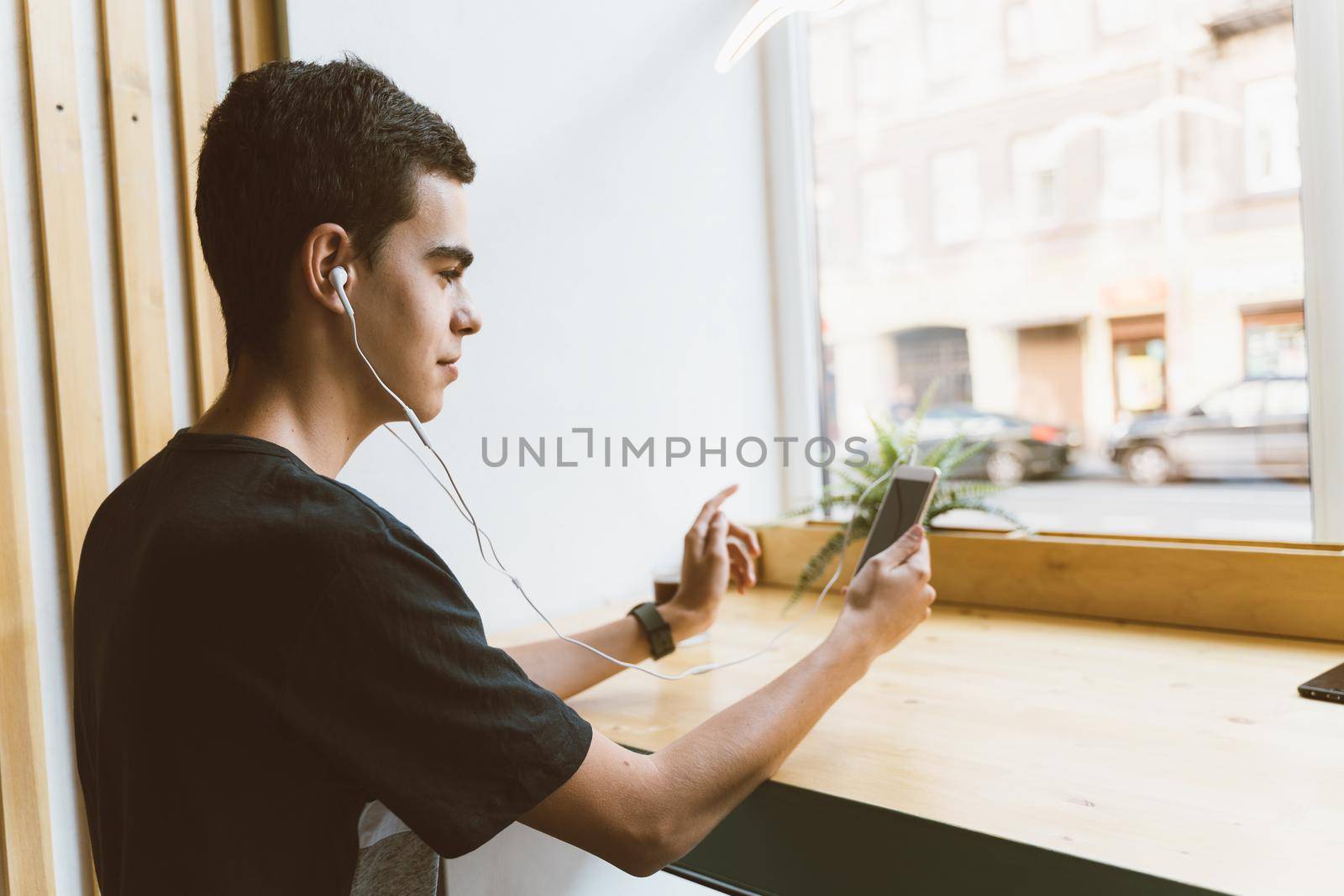 Young adult text message on smartphone and listen to music on a headphones in cafe. Lifestyle, free time, rest, relaxation