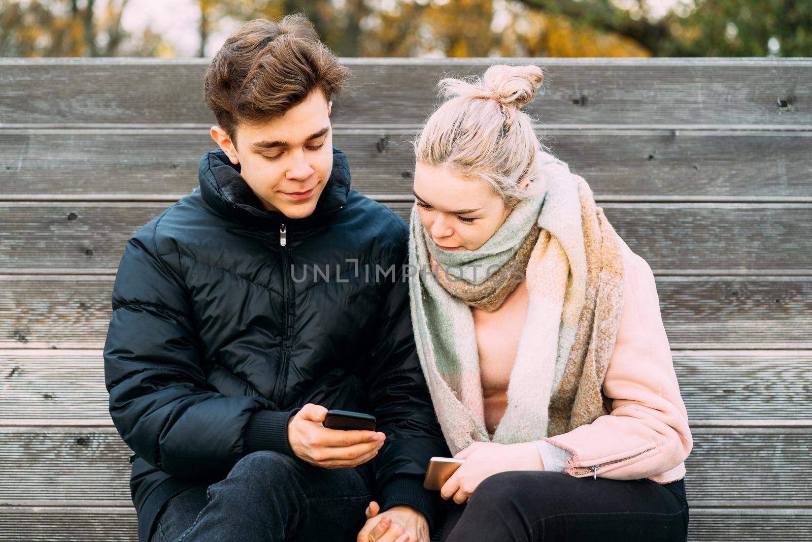 Loving teenagers on date look at mobile phones, guy shows the girl something interesting on the phone. Immersion in virtual world, social networks. Concept of teen love, Smombie dating