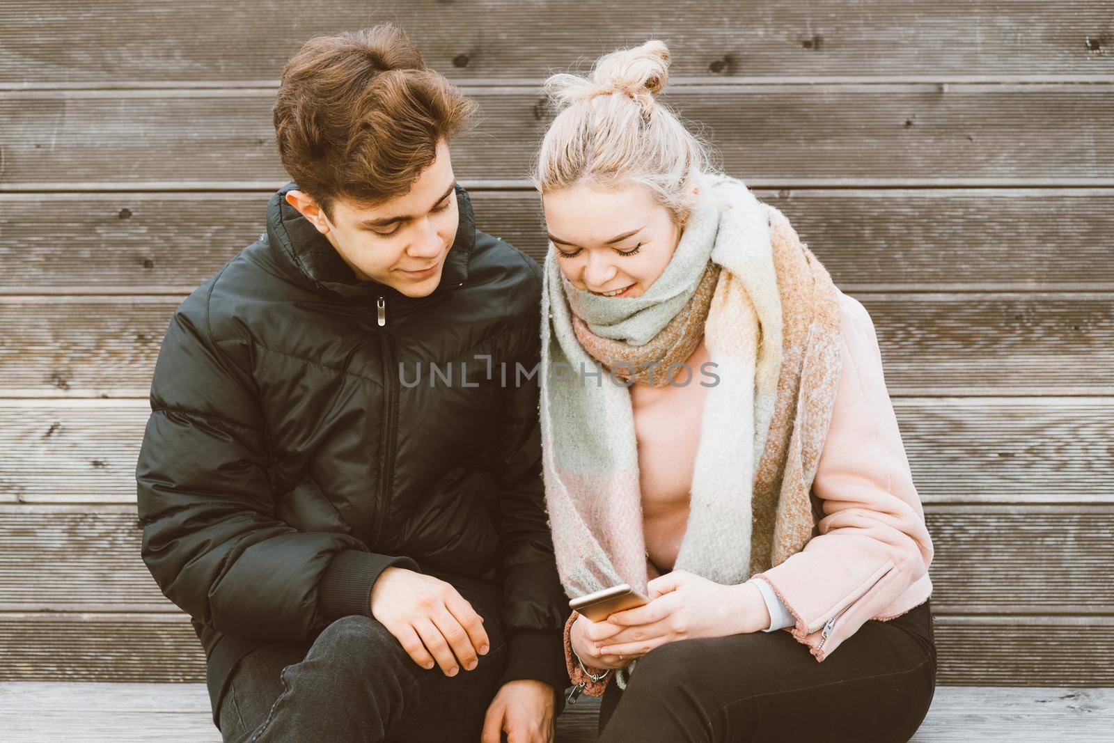 Loving teenagers on date look at mobile phones, girl shows guy something interesting on a mobile phone. Immersion in virtual world, social networks. Concept of a teen love, Smombie dating