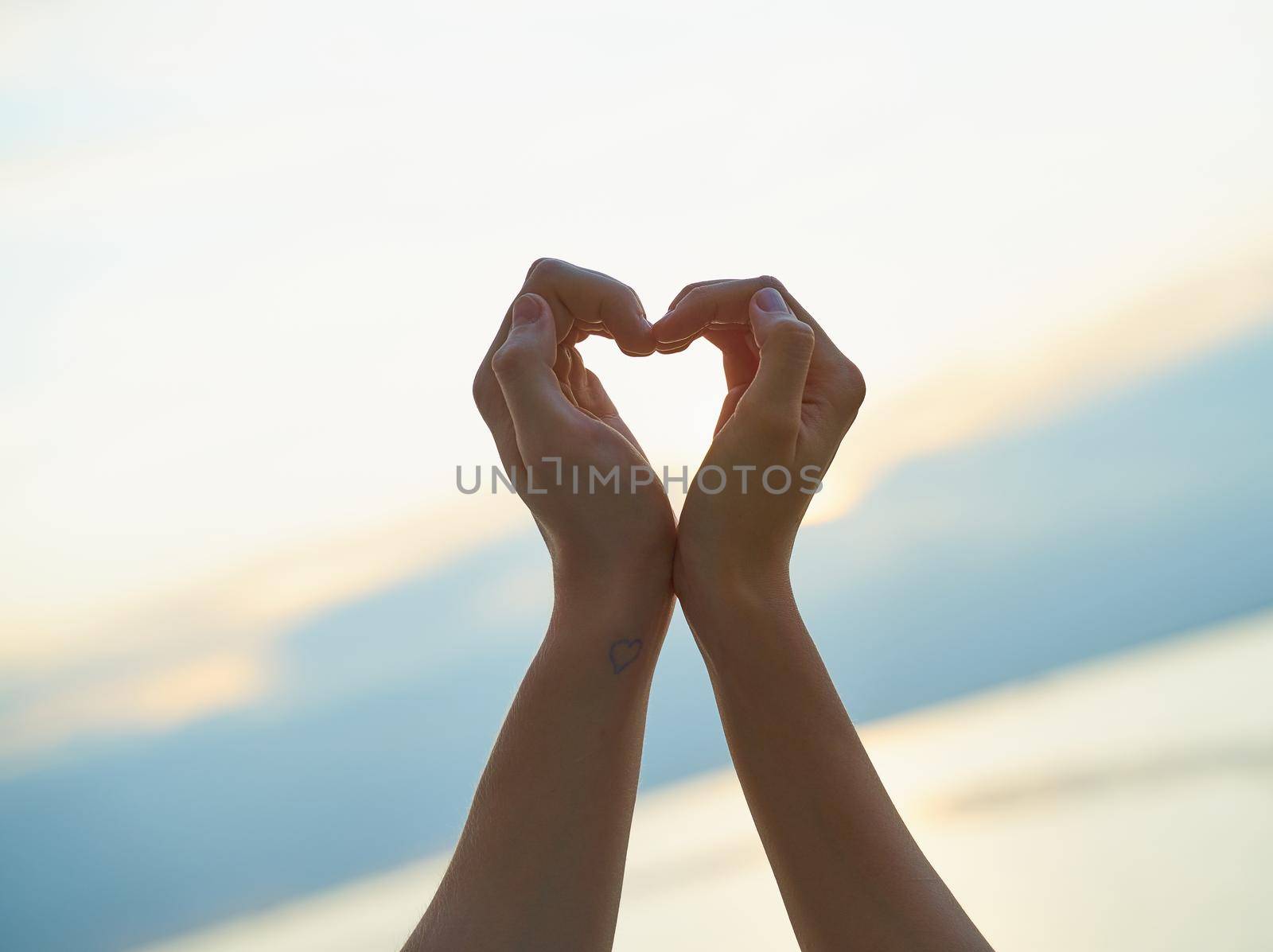 couple showing heart with hands, sign of love, ocean and sunset on background, evening sunset