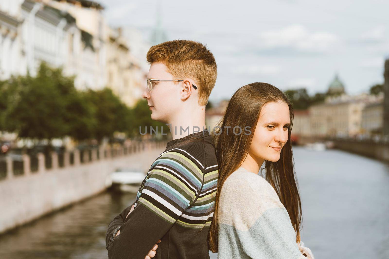 portrait of happy couple, standing back to back in the city center, red-haired man in glasses, beautiful woman with long dark hair by NataBene