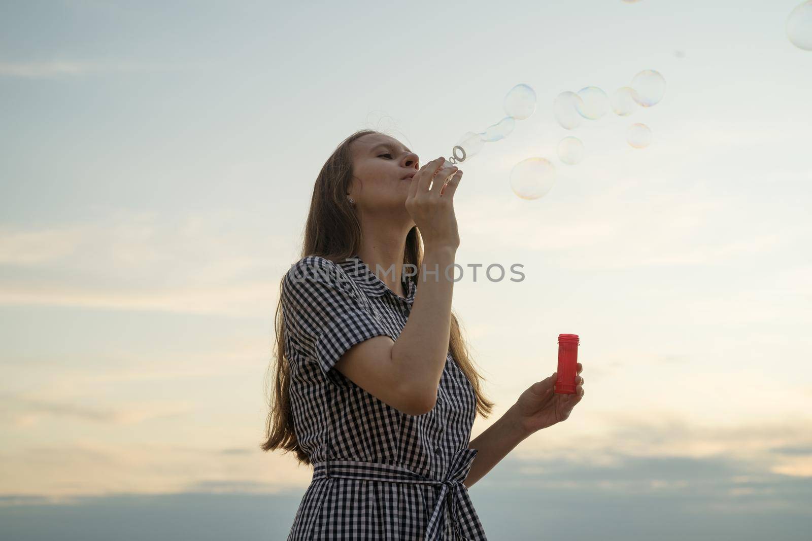 Teenager blowing soup bubbles, concept of fun and joy, sky and clouds on background by NataBene