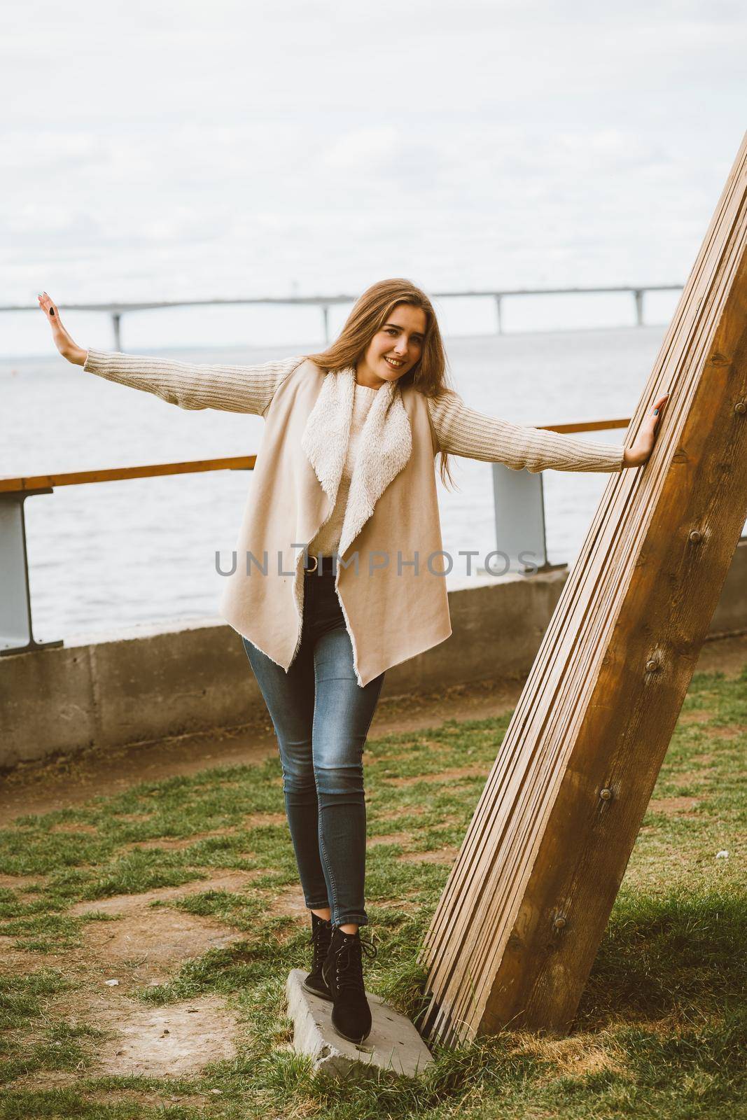 Happy young girl standing on waterfront at pier in port, enjoying life and waving his arms. Woman with long hair smiles and enjoys moment by NataBene