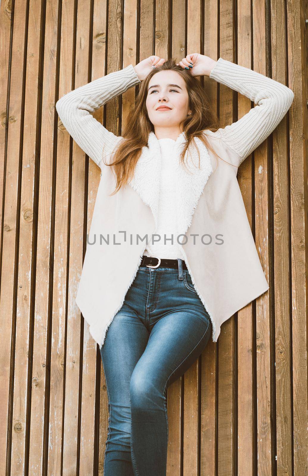 Portrait of beautiful young girl with long brown hair lying and relaxing on wooden background of planks, winter or autumn outdoor photoshoot with attractive woman by NataBene