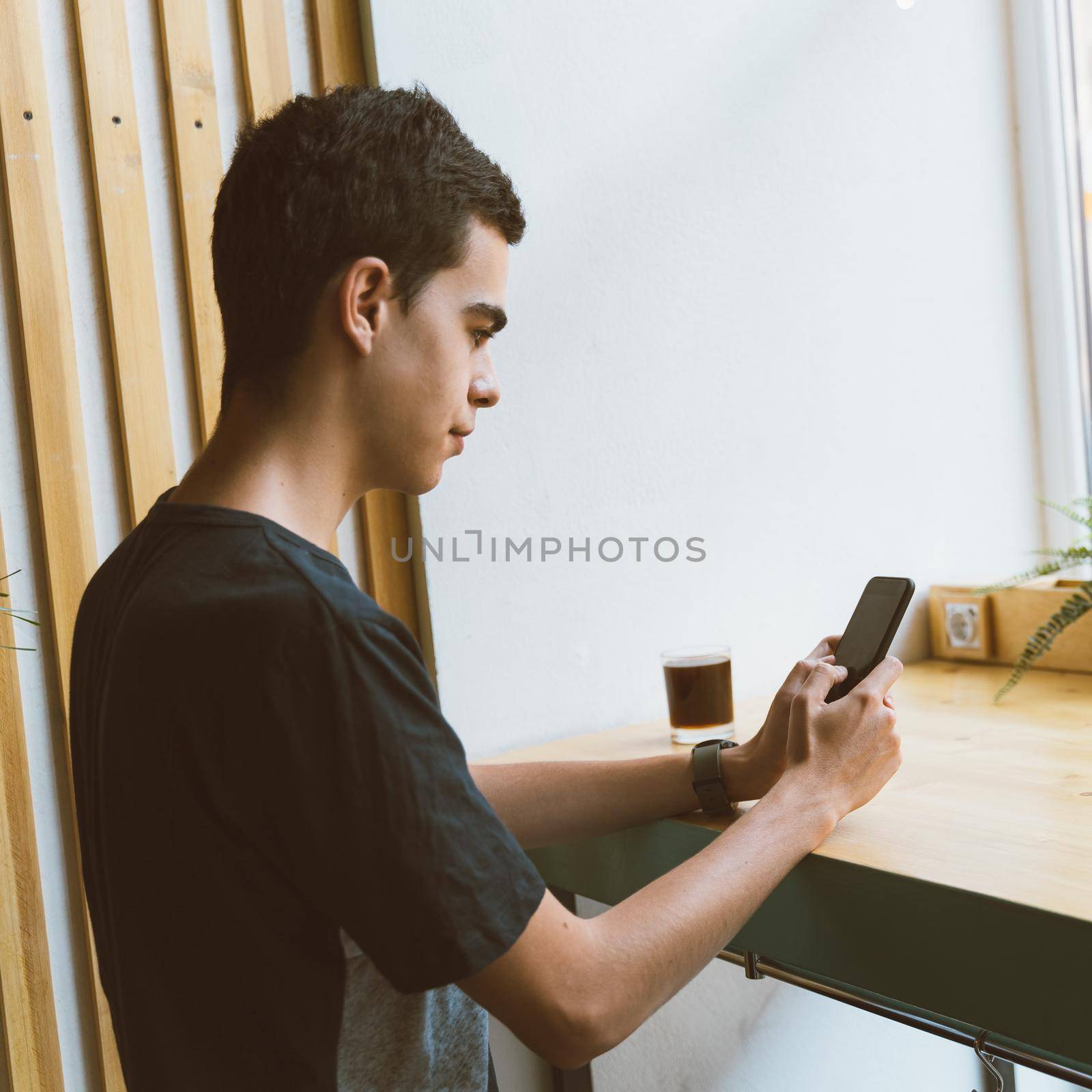 Young adult looking at mobile phone, sitting in a cafe. Lifestyle. Digital age. People communicate in chat, send sms. Copy space