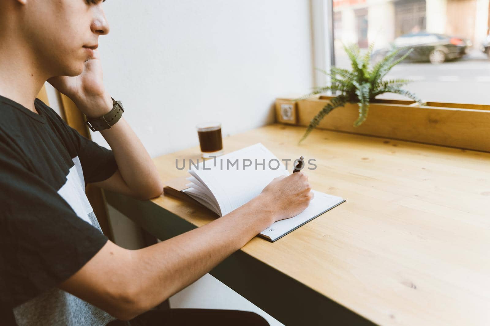 Young man writing information to notepad and speaking mobile phone, teenager in casual clothes plans schedule