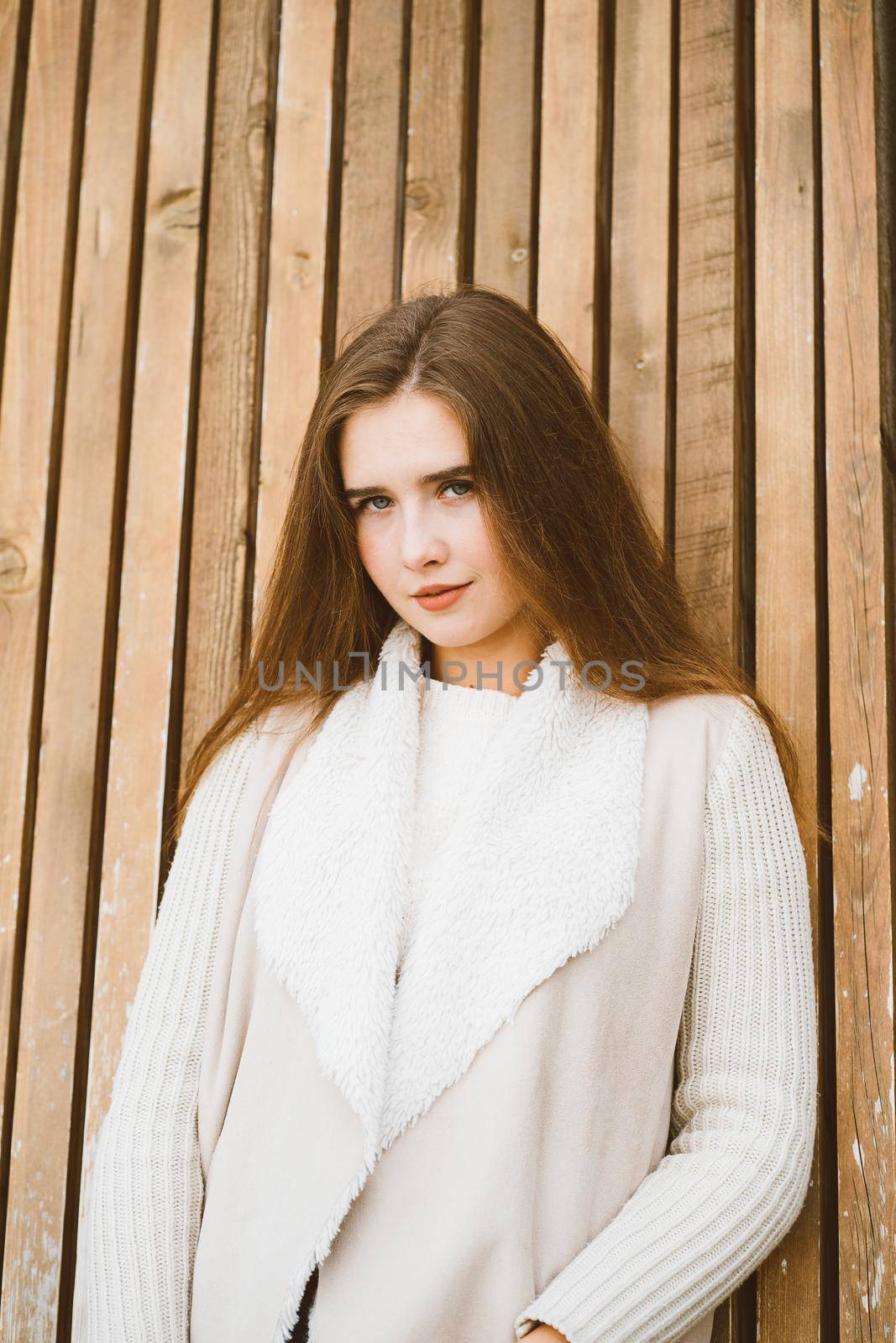 Close up portrait of beautiful young girl with long brown hair on the wooden background of planks, winter or autumn outdoor photoshoot with attractive woman, vertical