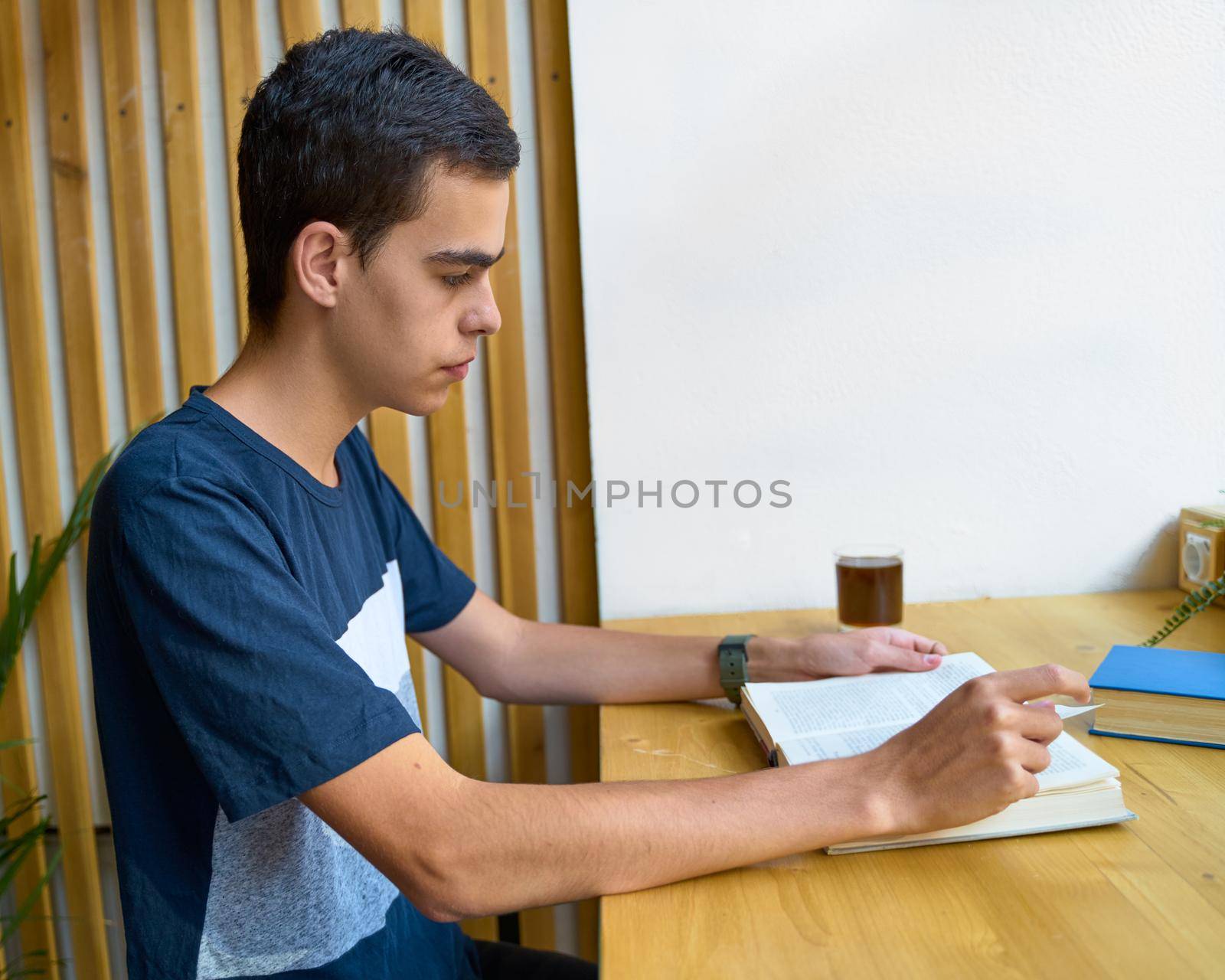 Young man with black hair reading a book, teenager in casual clothes in library, copy space