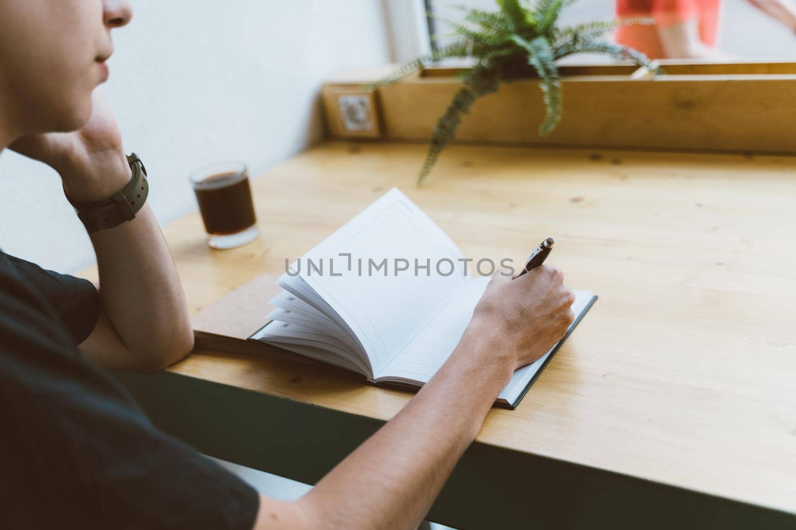 Young man writing information to notepad and speaking mobile phone, teenager in casual clothes plans a schedule by NataBene