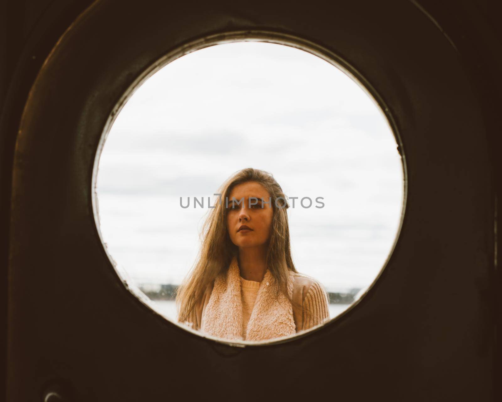 The face of young girl in round frame window on background of sea, ocean, on the waterfront. Portrait in circle, backlit