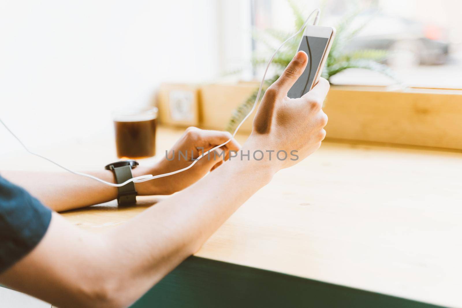 Young adult boy, man, unrecognizable person text message on smartphone and listen to music on headphones in cafe. Lifestyle, free time, rest, relaxation by NataBene