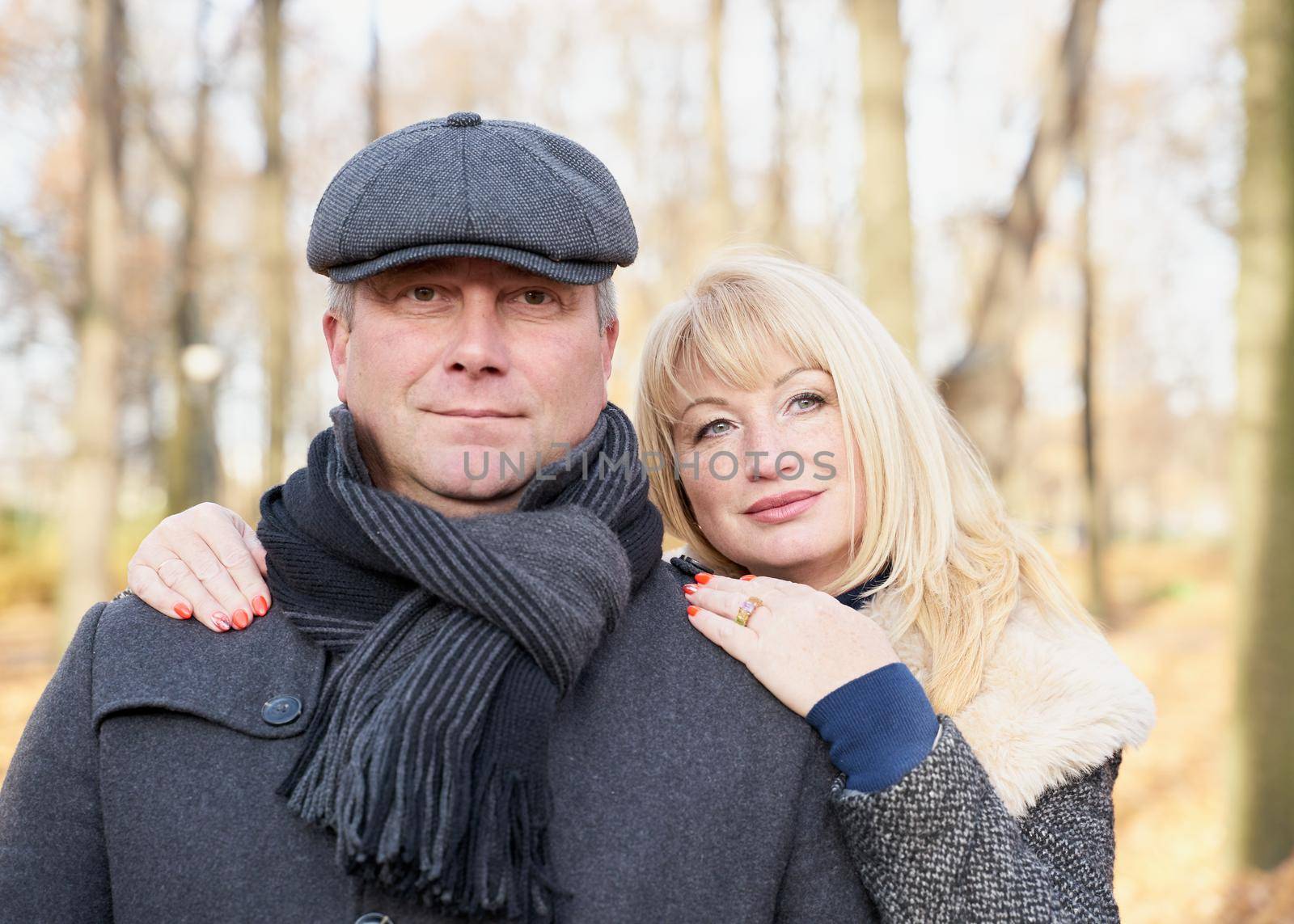 Closeup portrait of happy blonde mature woman and beautiful middle-aged brunette, looking looking directly at the camera. Loving couple of 45-50 years old walks in autumn park in warm clothes