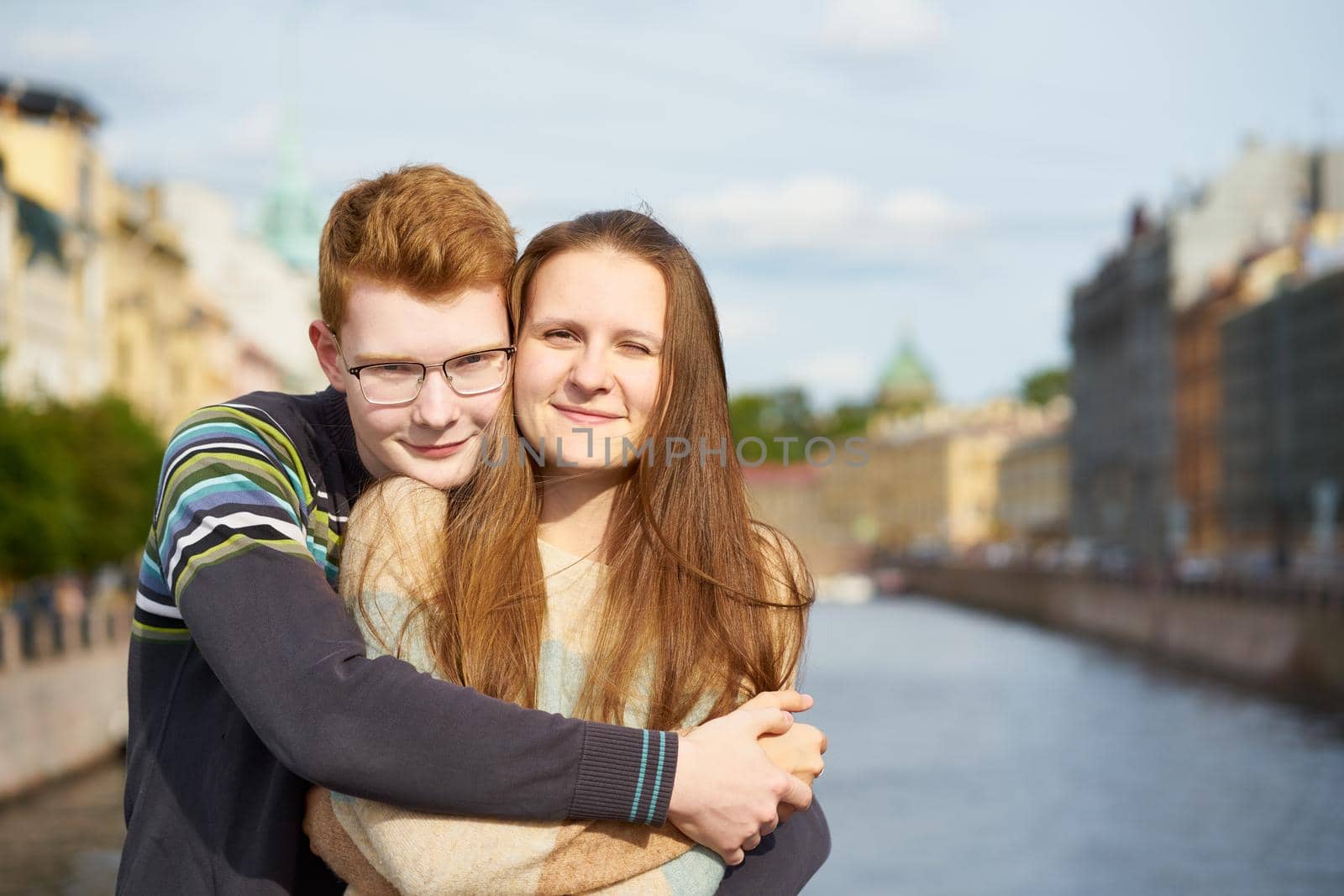 portrait of happy couple embracing in downtown, red-haired man with glasses, woman with long hair looking straight by NataBene