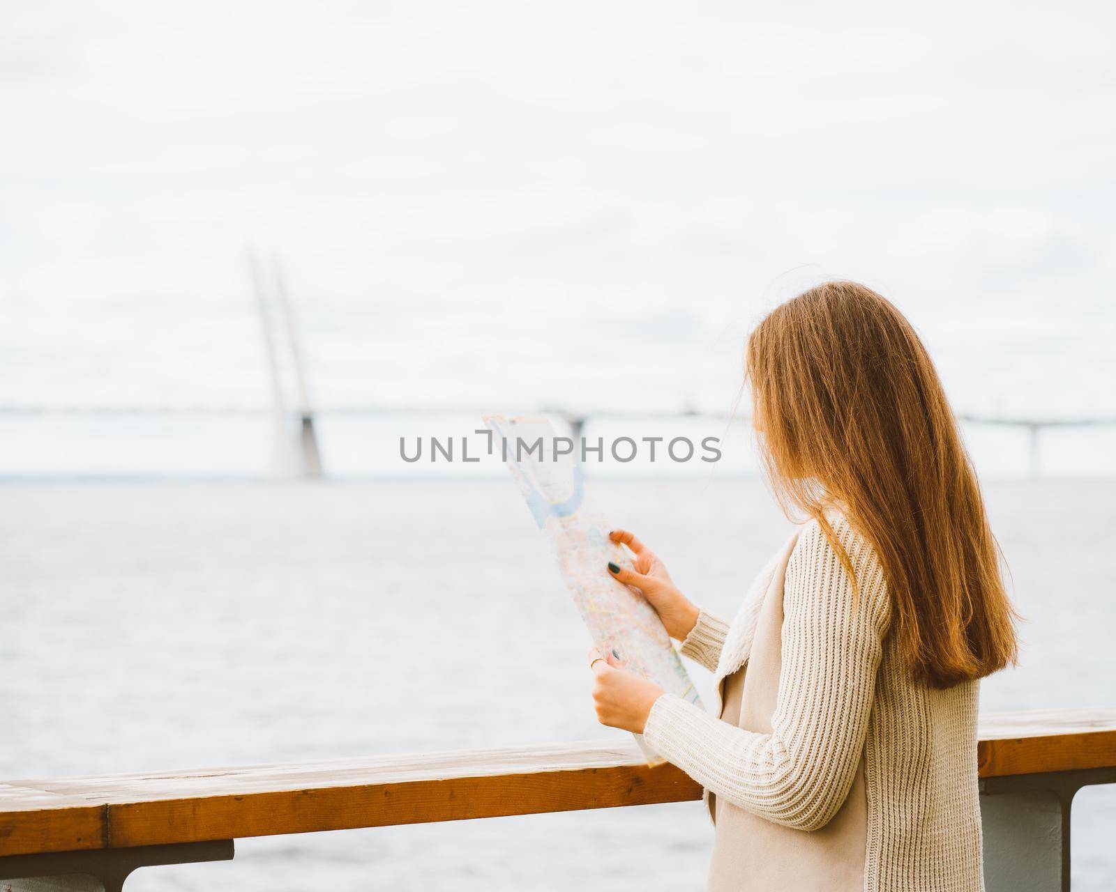 Young woman standing on waterfront of a big city and looking at guide, a tourist in port looking for for attractions and waiting for ferry