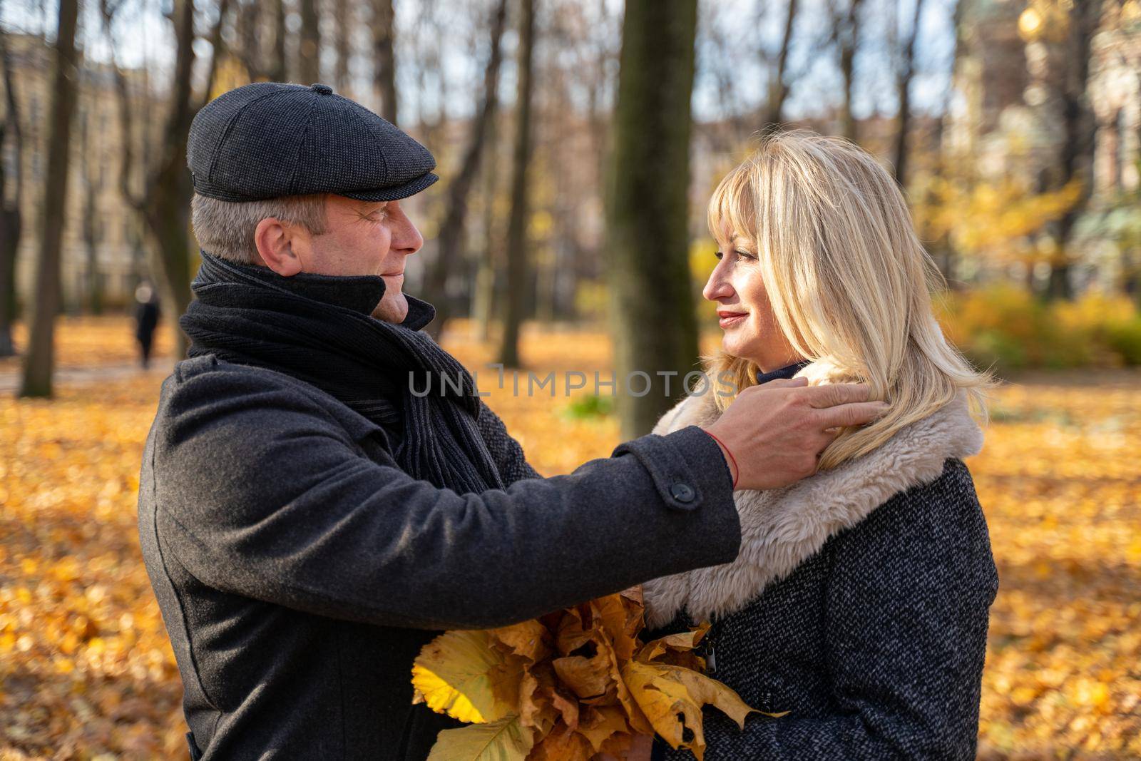 Handsome brunette middle-aged man carefully adjusts his hair. Happy blonde mature woman. Loving couple 45-50 years old are walking in the park, looking at each other