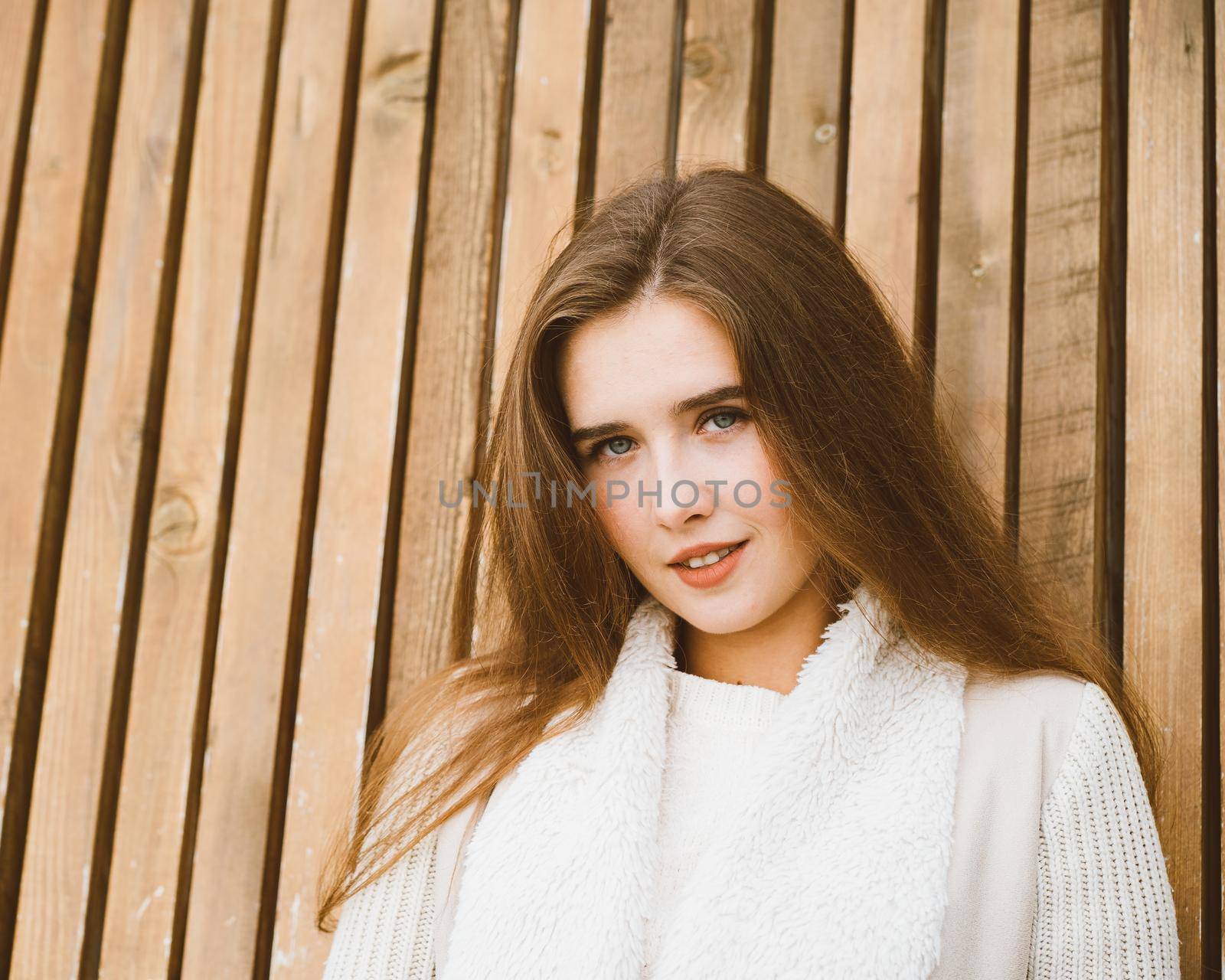 Close up portrait of beautiful young girl with long brown hair on wooden background of planks, winter or autumn outdoor photoshoot with attractive woman by NataBene