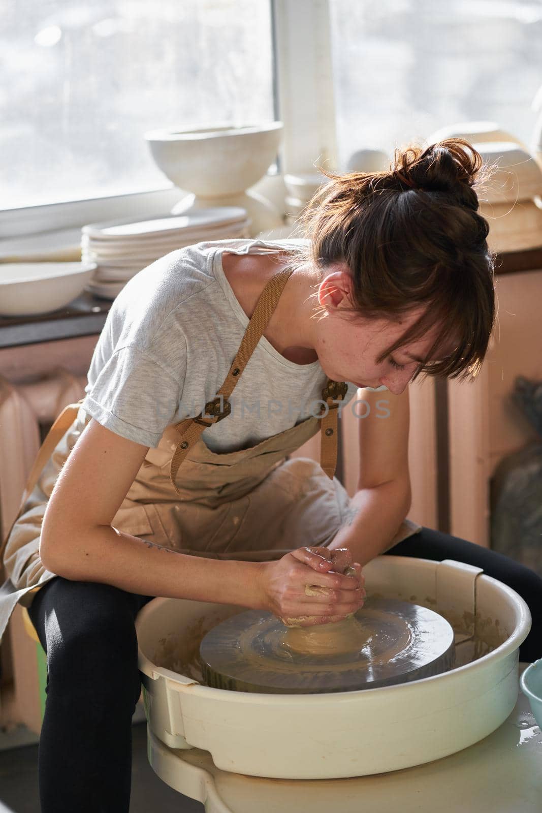 Woman making ceramic pottery on wheel, sun light. Concept for working woman in freelance, business, hobby