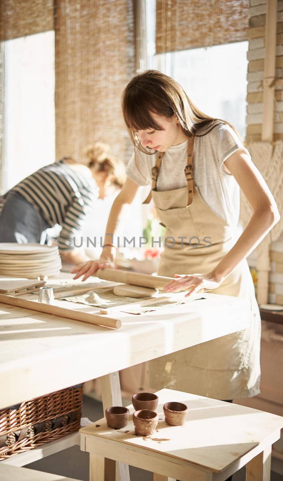 Beautiful young woman making ceramic ware, roll out with a rolling pin in sun light. Concept for woman in freelance, business, hobby