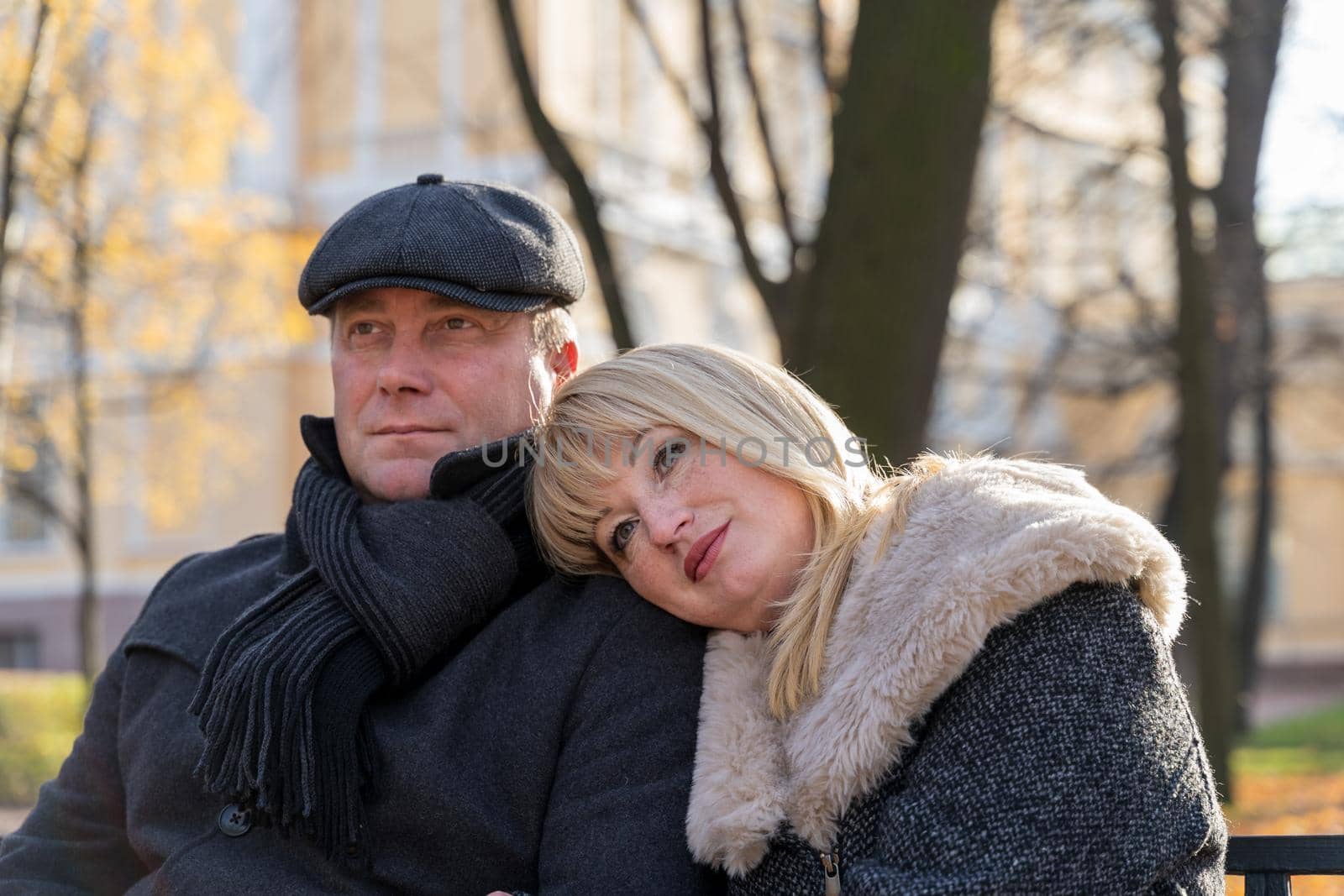 Closeup portrait of happy blonde mature woman and beautiful middle-aged brunette, looking away. Loving couple of 45-50 years old walks in the autumn park in warm clothes, in coat and enjoys life