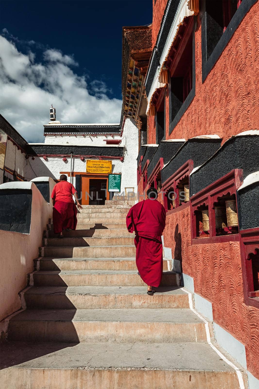 THIKSEY, INDIA - SEPTEMBER 13, 2012: Young Buddhist monks walking on stairs along prayer wheels in Thiksey gompa Tibetan Buddhist monastery, Ladakh, India