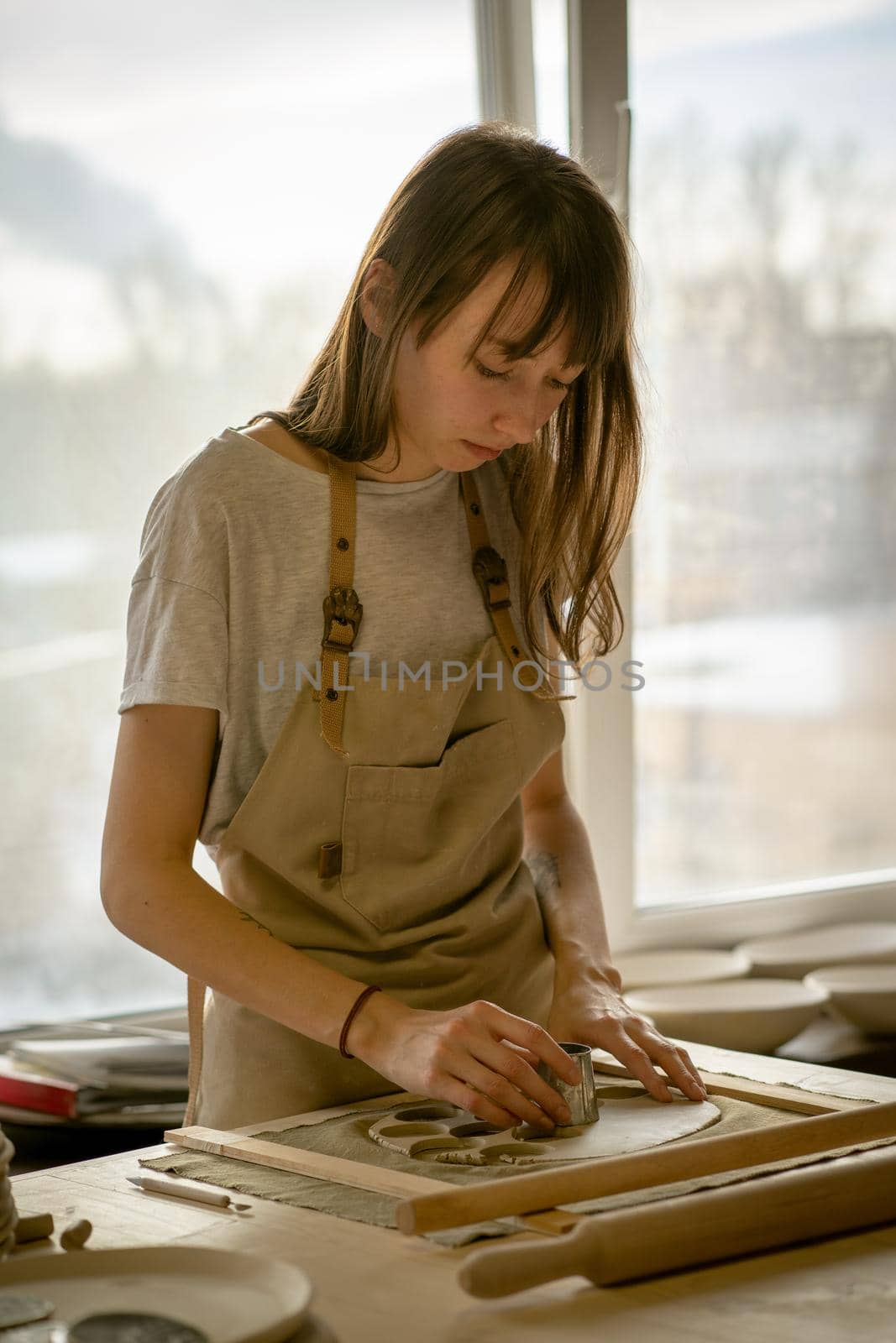 Beautiful young woman making ceramic ware, molding a shape in workplace in sun light. Concept for woman in freelance, business, hobby