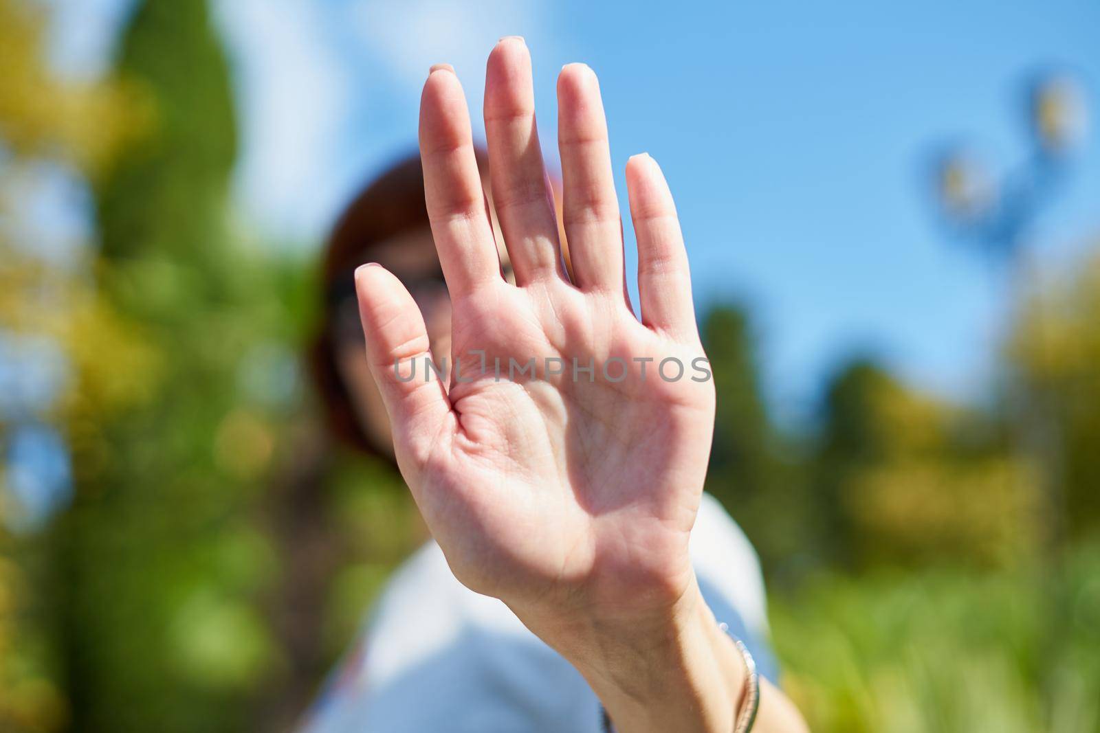 Unrecognizable woman shielding her face from camera. Selective focus. Concept of privacy, personal space, prohibition of photography. Female on summer sunny day. Stop, taking pictures is forbidden