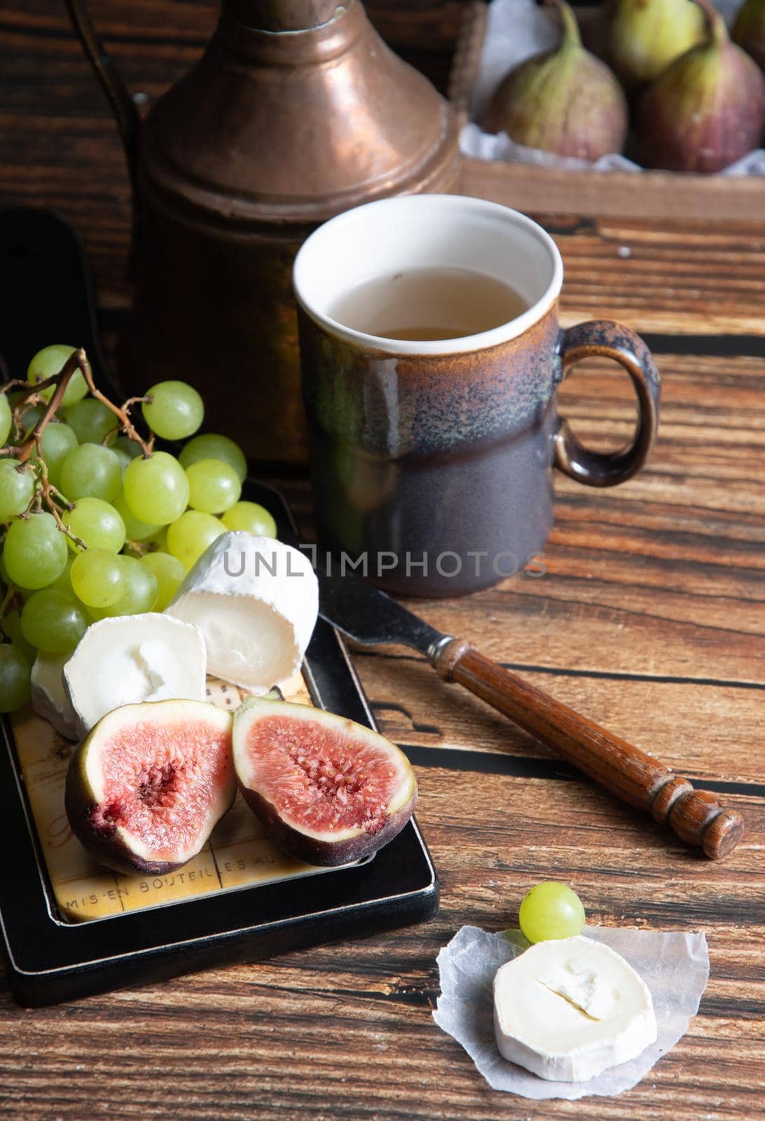 cheese plate with goat cheese, grapes and figs, copper teapot, angle view, healthy food, high-calorie breakfast. High quality photo