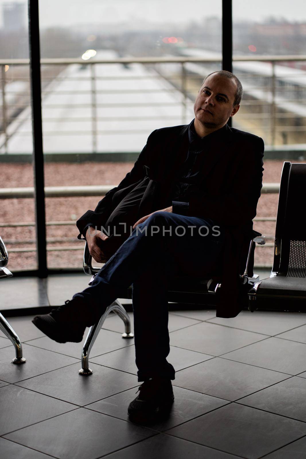 Train Station. A mature man in business clothes and a coat is sitting in a waiting room by NataBene
