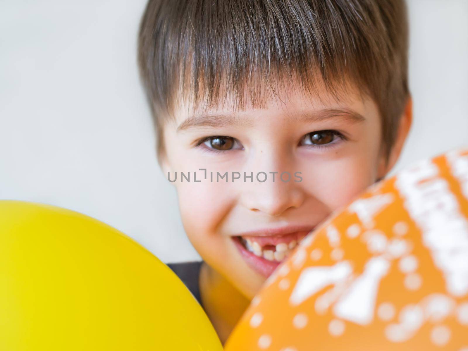 Smiling kid shows hole in row of teeth in his mouth. One incisor fell out just now. Happy child with air balloons. by aksenovko