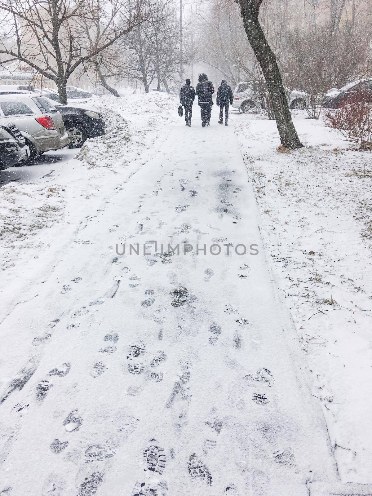 Three men walk down the street covered with snow. Footprints on snowy pavement. Winter in town. by aksenovko