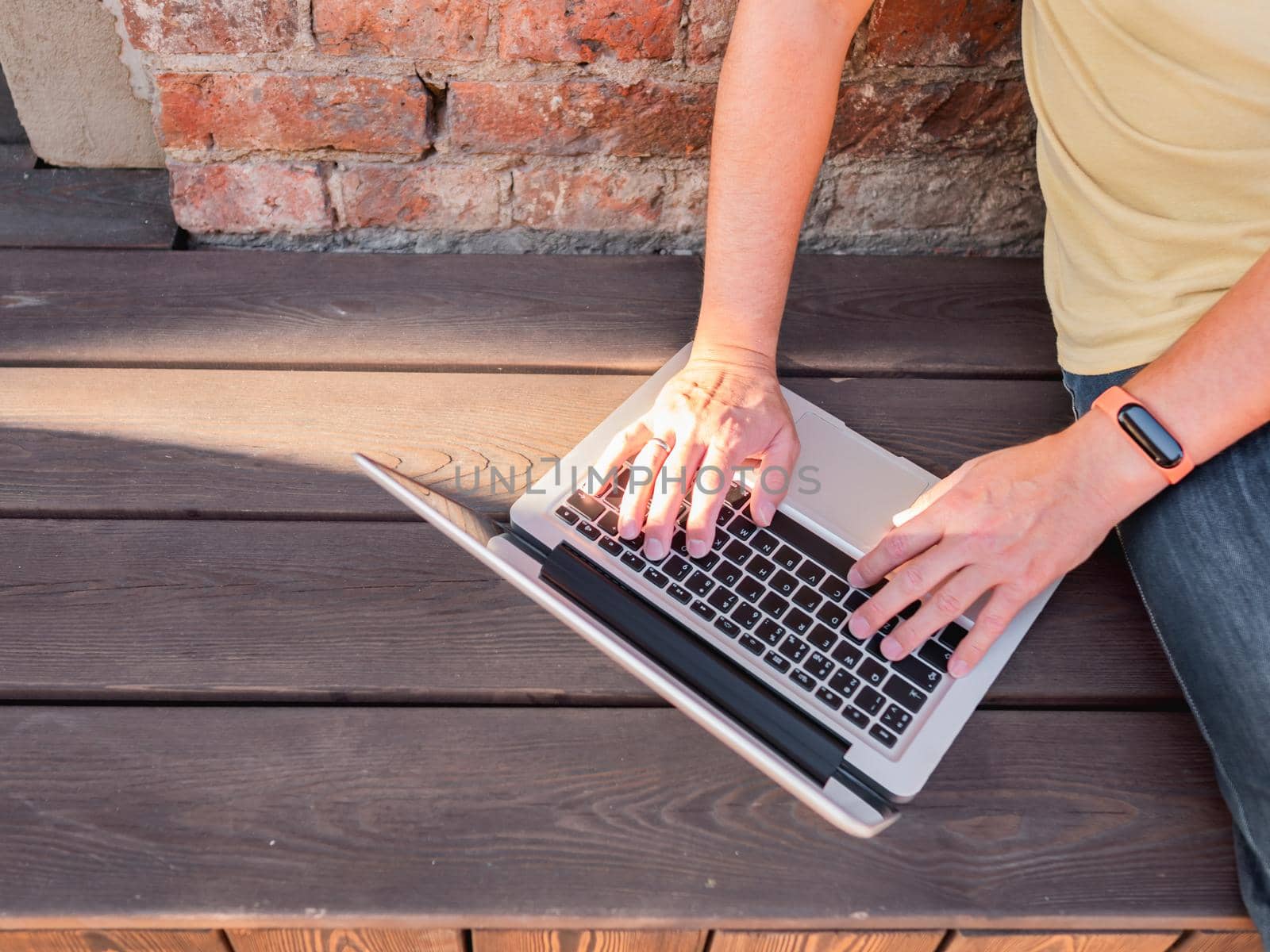 Top view on man's hands on computer keyboard. Freelancer works outdoors with laptop. Modern lifestyle. Open air workplace. by aksenovko