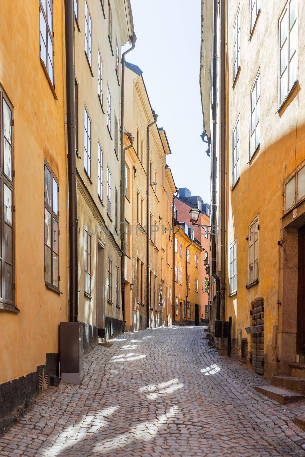 Bright sun reflections on narrow street in historic part of Stockholm. Old fashioned building in Gamla stan, old part of town. Sweden. by aksenovko