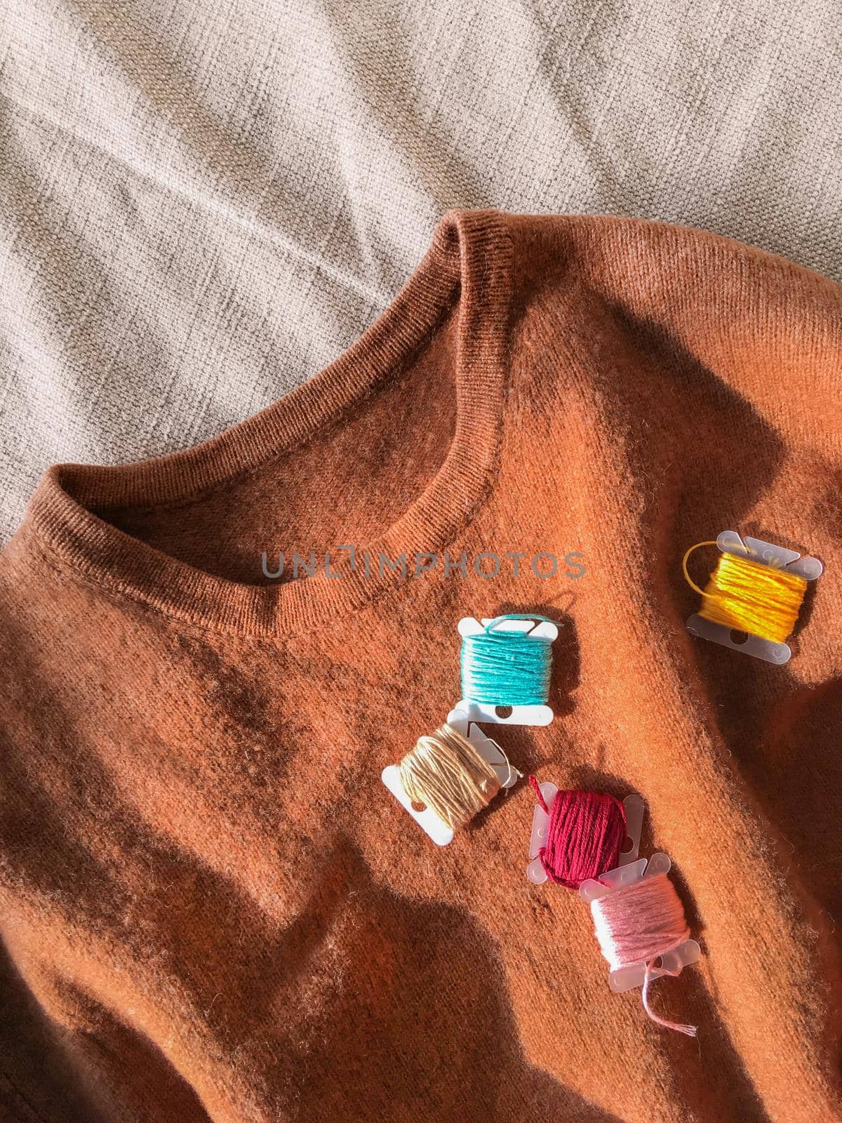 Top view on earth toned wool sweater and coils of colorful embroidery threads. Remaking old clothes. DIY. Handmade craft. by aksenovko