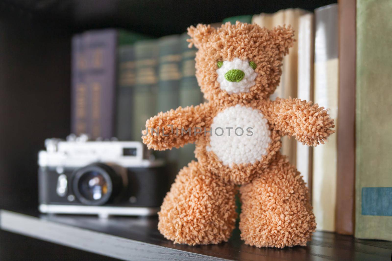 Hand made teddy bear on bookshelf. Crocheted brown toy for children. Cute souvenir, handicraft product. by aksenovko