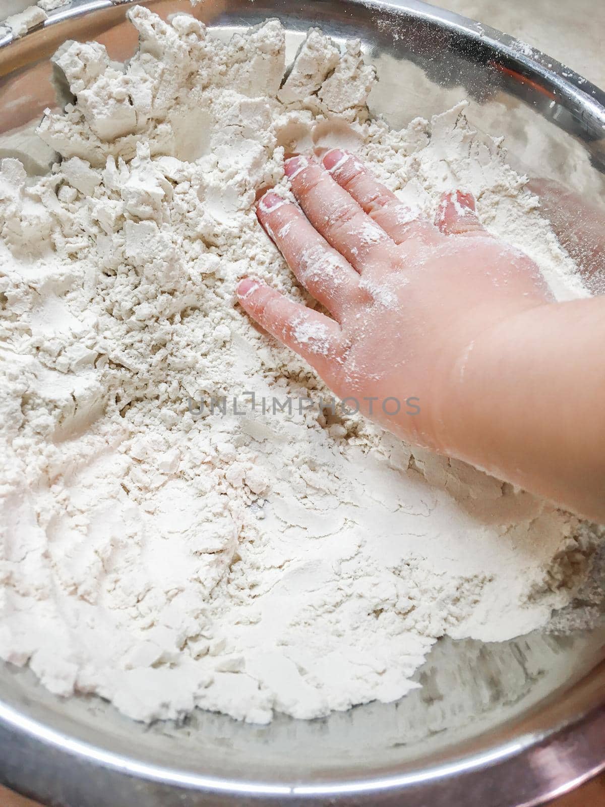 Little child is touching flour in metal bowl. Cooking with children. Developing fine motor skills by letting to touch food ingredients. by aksenovko