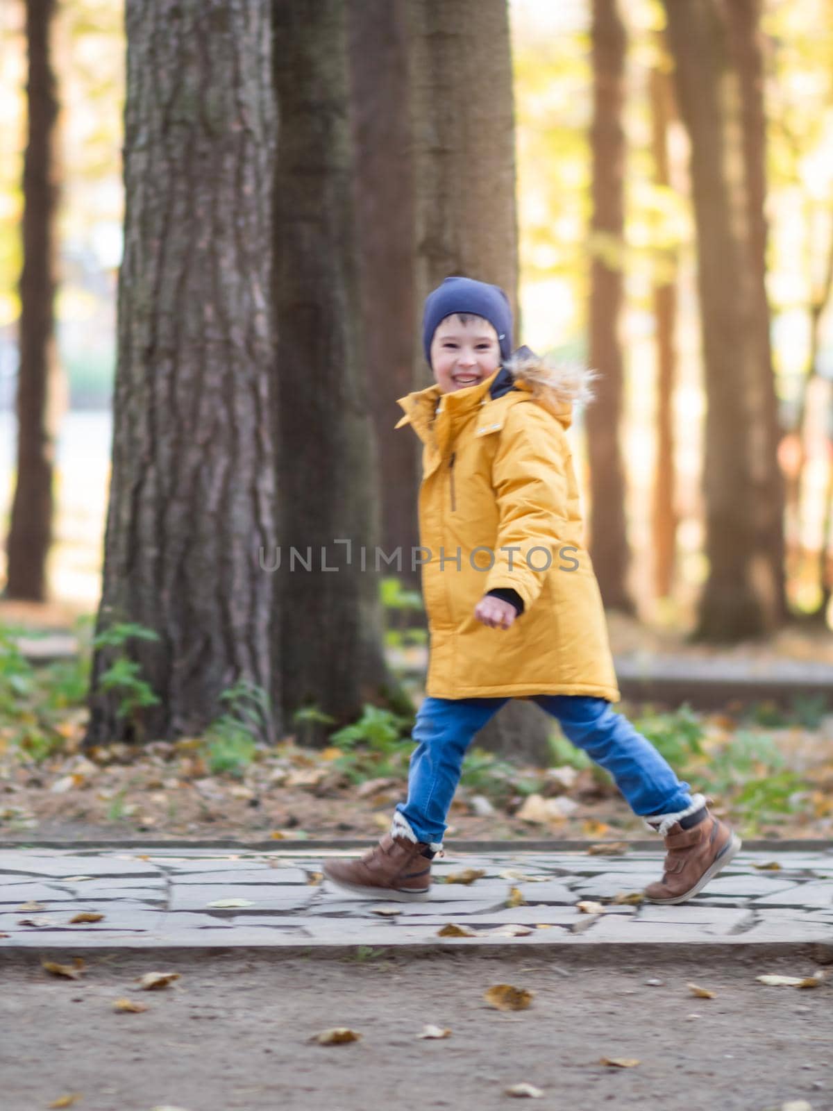 Little boy in yellow jacket runs on walking path at park. Autumn sunny day. Leisure activity outdoors. Soft focus. by aksenovko