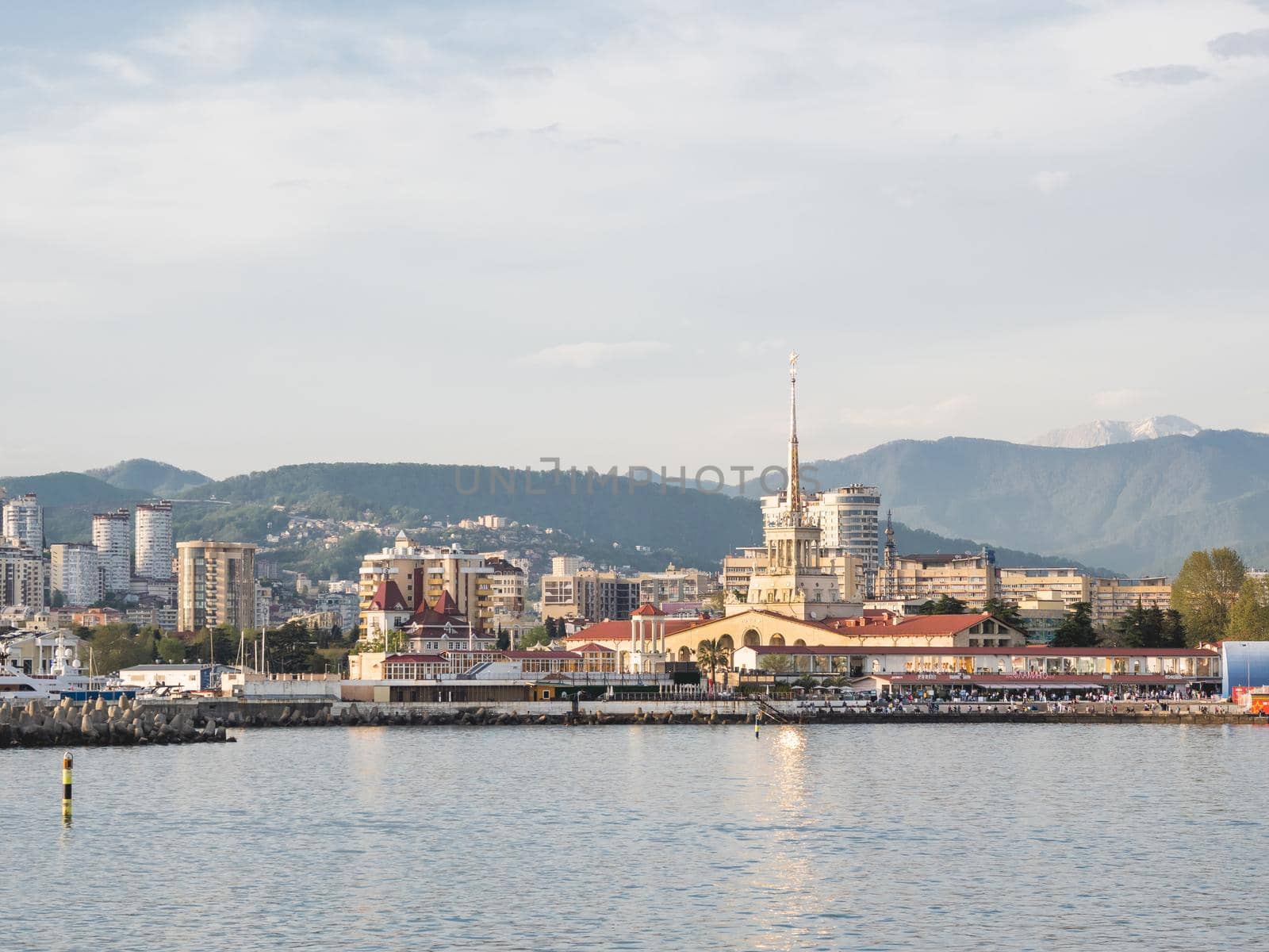 SOCHI, RUSSIA - May 03, 2021. Port of Sochi, sea embankment and residential district at sunset. View from Black sea in sunny weather. by aksenovko