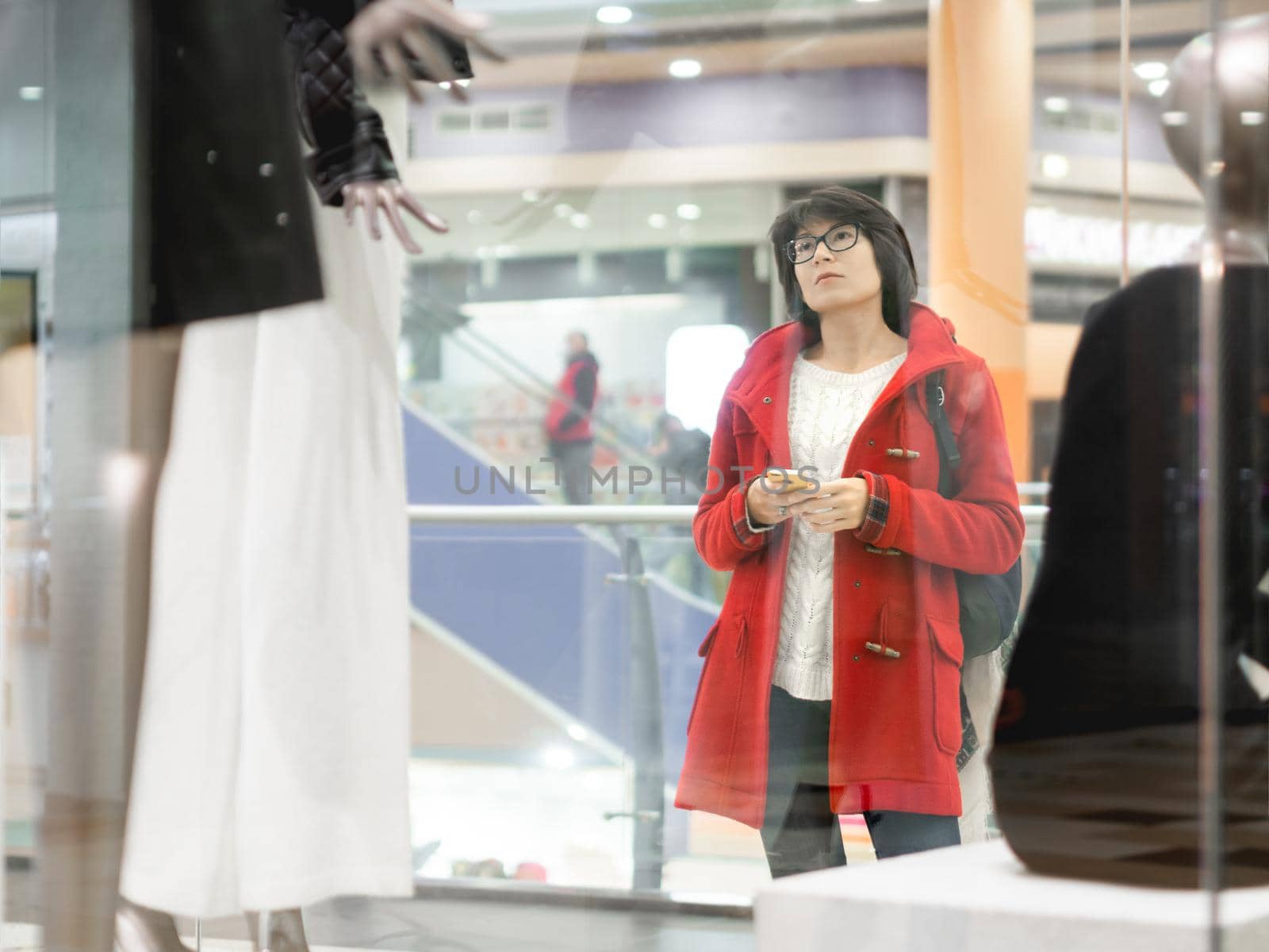 Woman stares on dummies in clothing store. Casual outfit hanging on mannequins. View through transparent shop window. Shopping at mall. Basic clothes for everyday wear. Modern urban fashion. by aksenovko