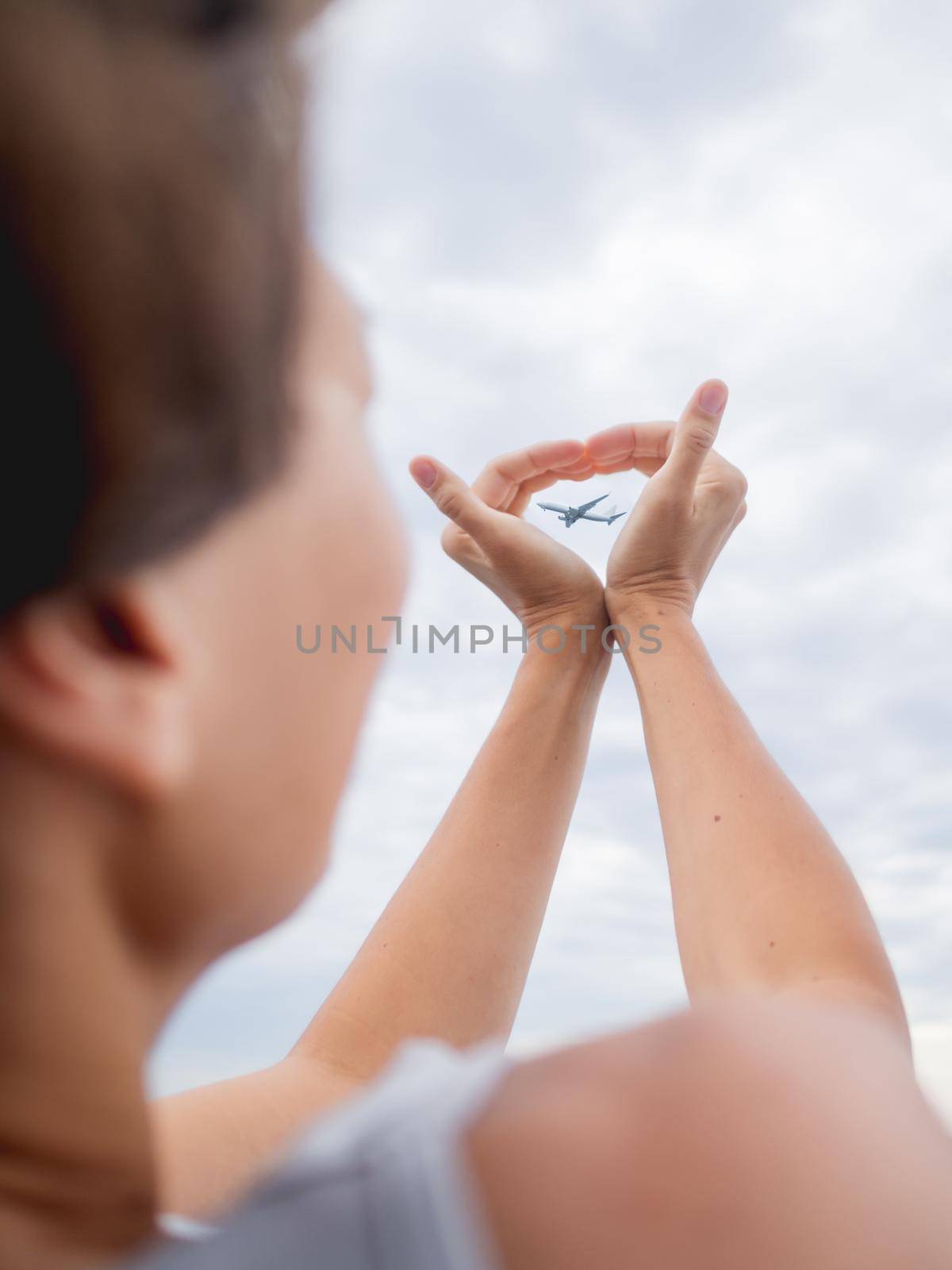 Woman makes heart symbol with flying plane in it. Romantic gesture of wanderlust. Travel by plane concept.