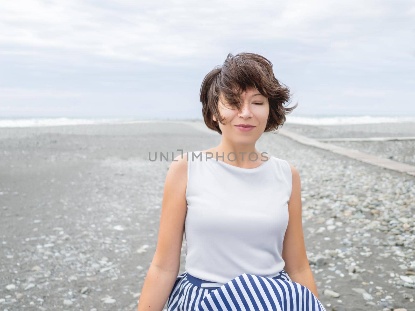 Portrait of smiling woman on seaside. Woman with hair ruffled with the wind. Wanderlust concept. Vacation on sea coast. by aksenovko