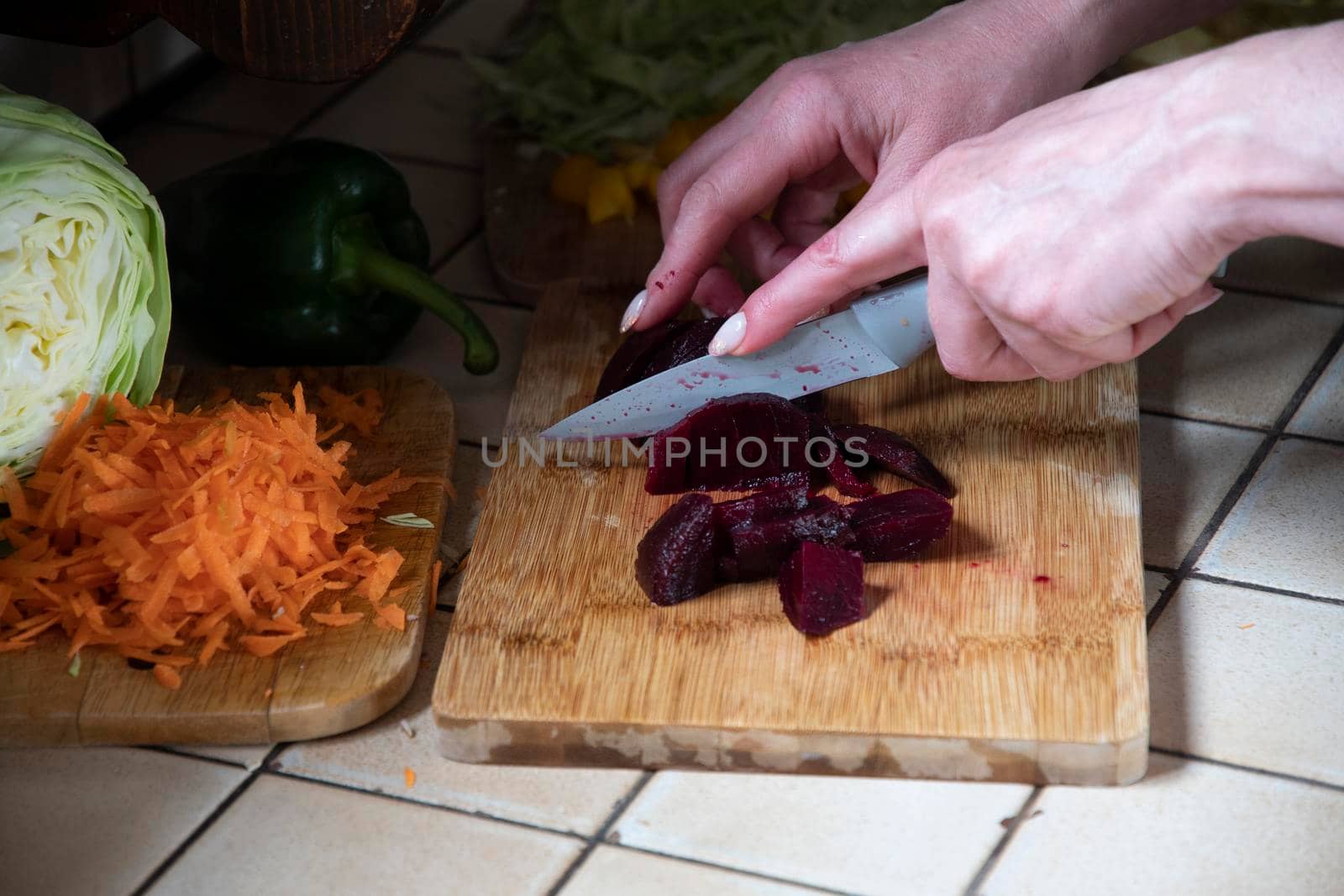 a woman cuts beets in the kitchen against the background of fresh vegetables, ingredients for step by step cooking soup. High quality photo