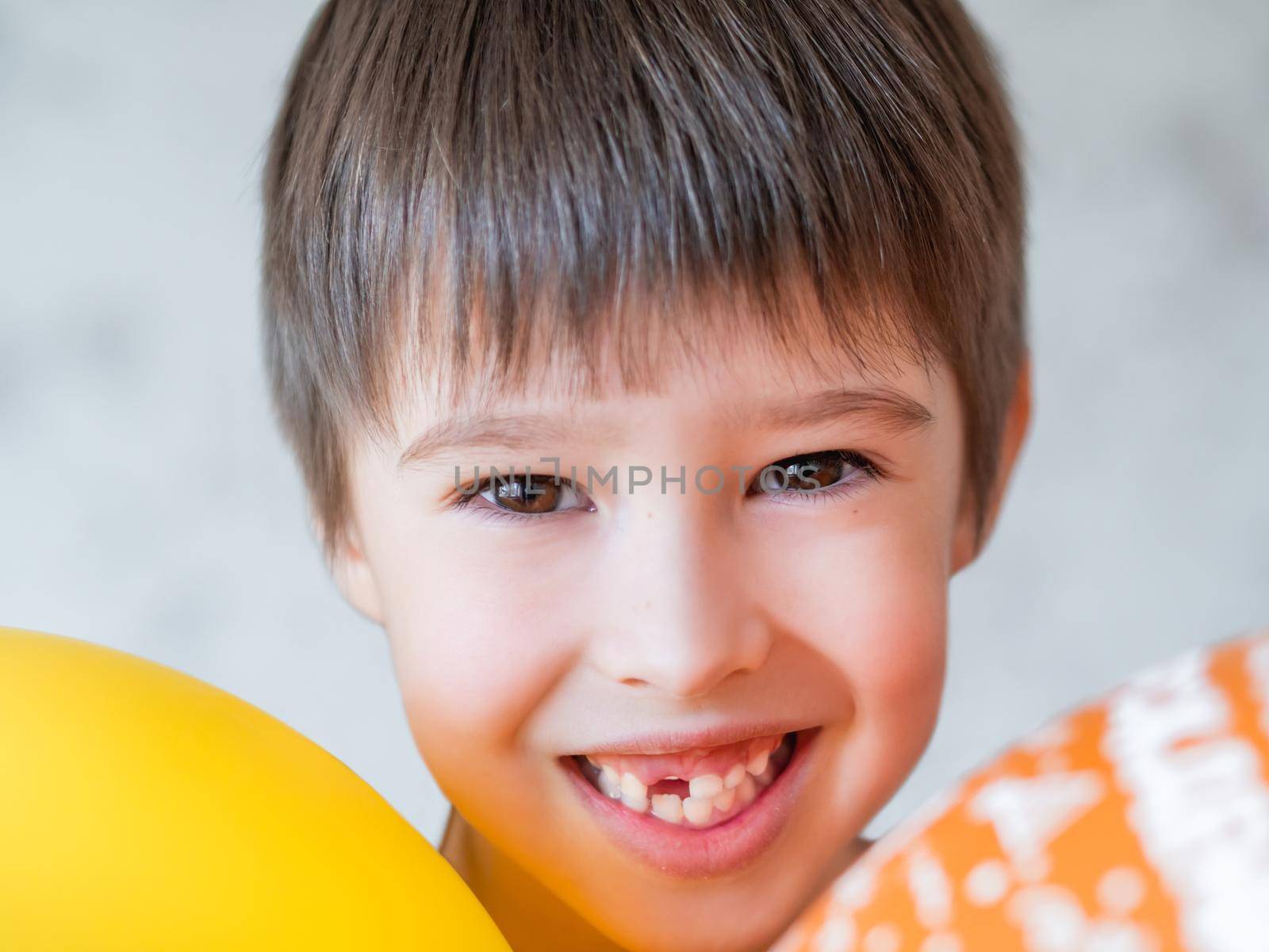 Smiling kid shows hole in row of teeth in his mouth. One incisor fell out just now. Happy child with air balloons. by aksenovko