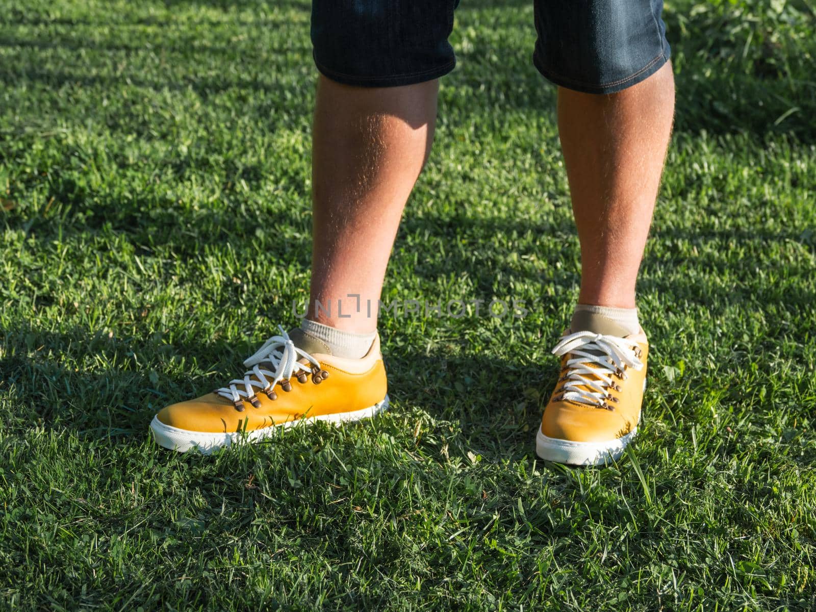 Man in bright yellow sneakers is standing on green grass lawn in park. Modern hipster's shoes. Urban fashion. by aksenovko