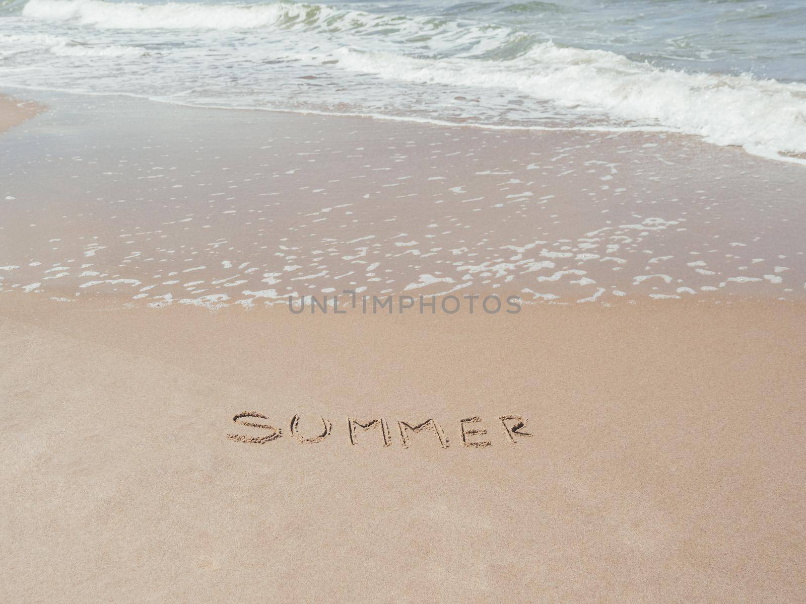 Sea coast with soft surf. Word SUMMER written on sandy beach. Summer vacation on seaside.