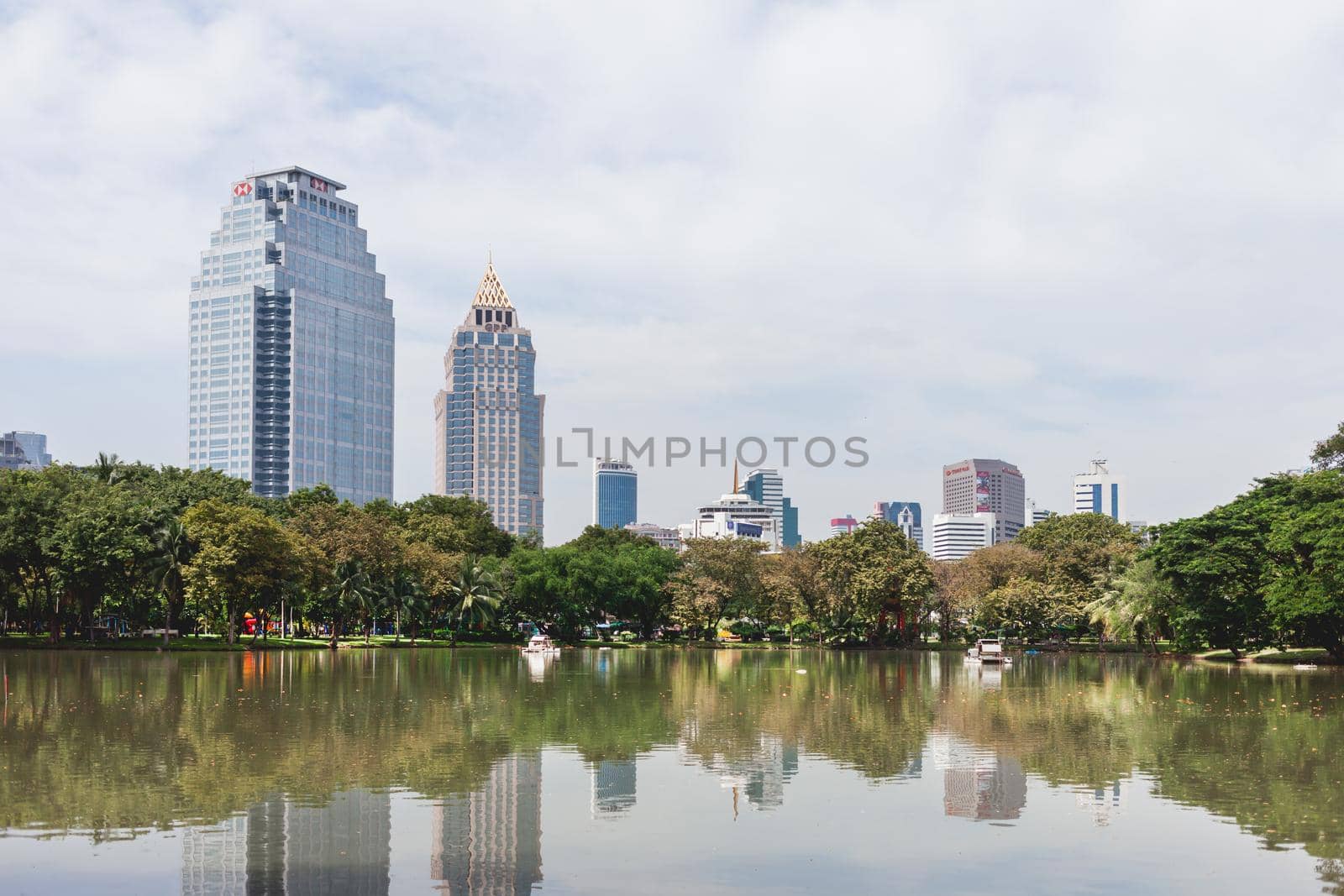BANGKOK, THAILAND - October 23, 2012. Panorama of downtown skyscrapers from Lumpini park. Daylight view over pond in recreation park. by aksenovko