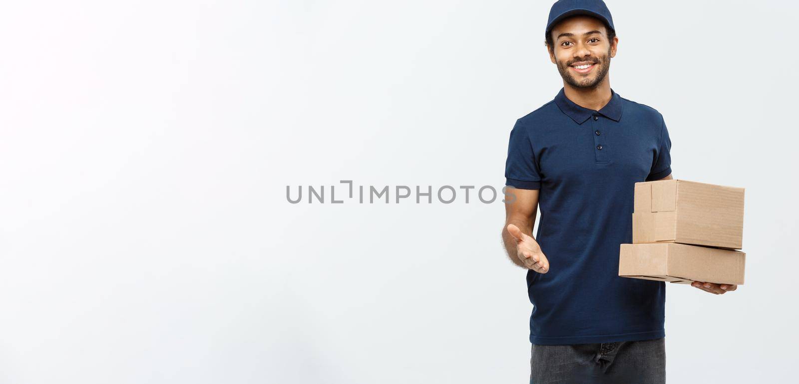 Delivery Concept - Portrait of Happy African American delivery man pointing hand to present box packages. Isolated on Grey studio Background. Copy Space