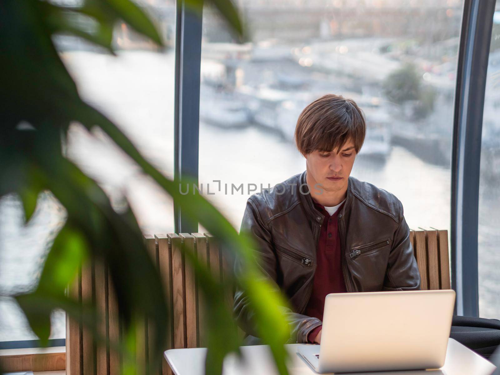 Businessman works with laptop and paper organiser in co-working center. Workplace for freelancers in business center. Sun is shining through panoramic window behind man.