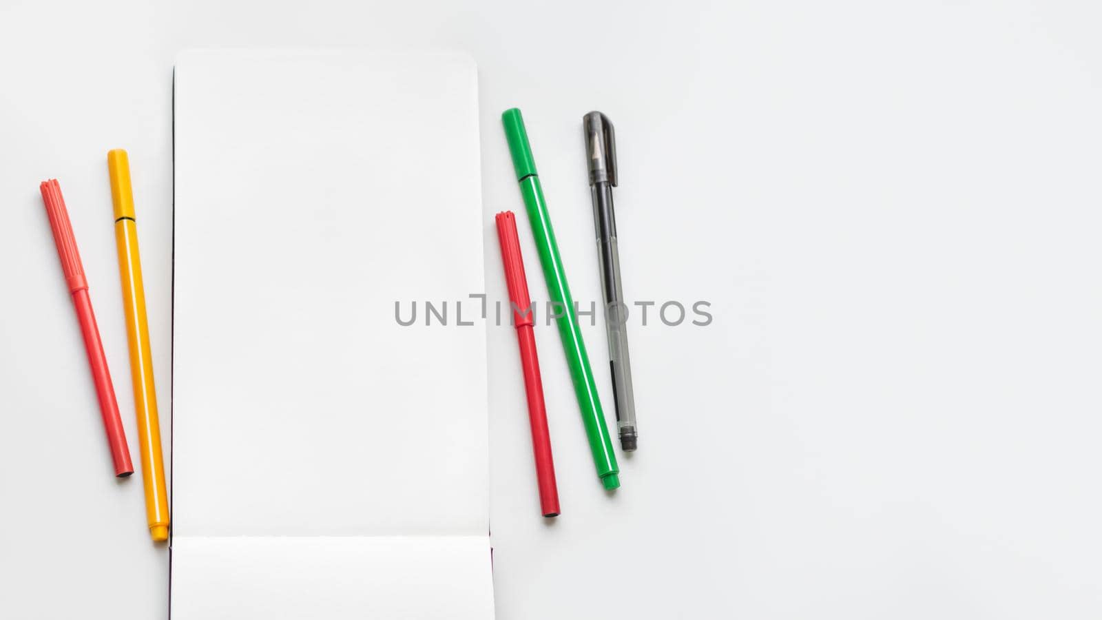 Top view on clear page of notebook. Mock up photo with notepad and colorful markers on white table. Workplace of artist. by aksenovko